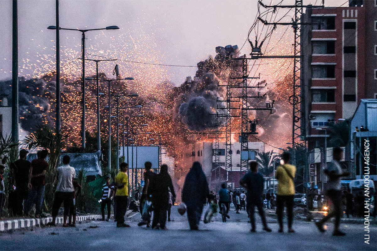 Dramatic explosion with bursts of flames and sparks in a crowded urban street, people in the foreground observing the event.