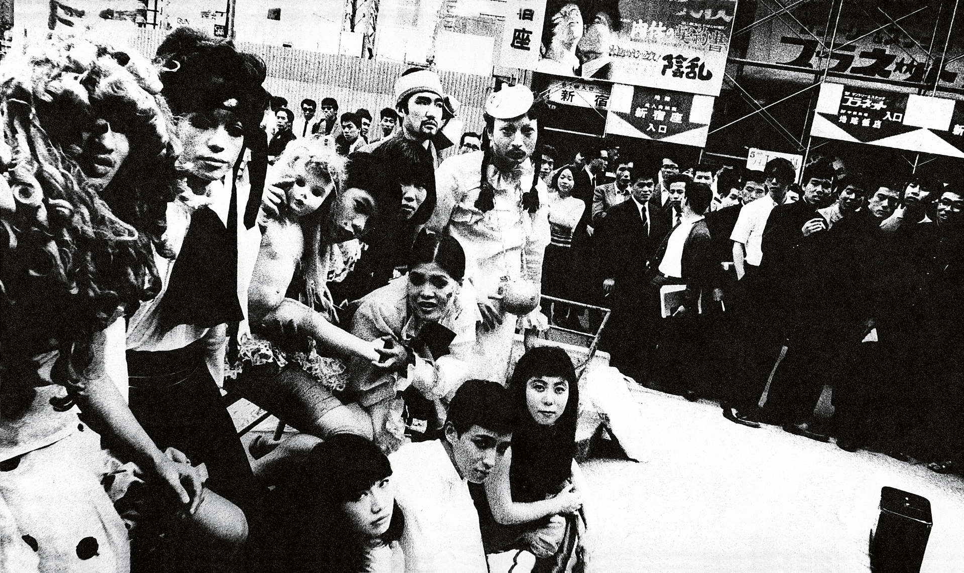 Black and white image showing crowded trading floor with people in suits gathered around trading stations and monitors overhead.