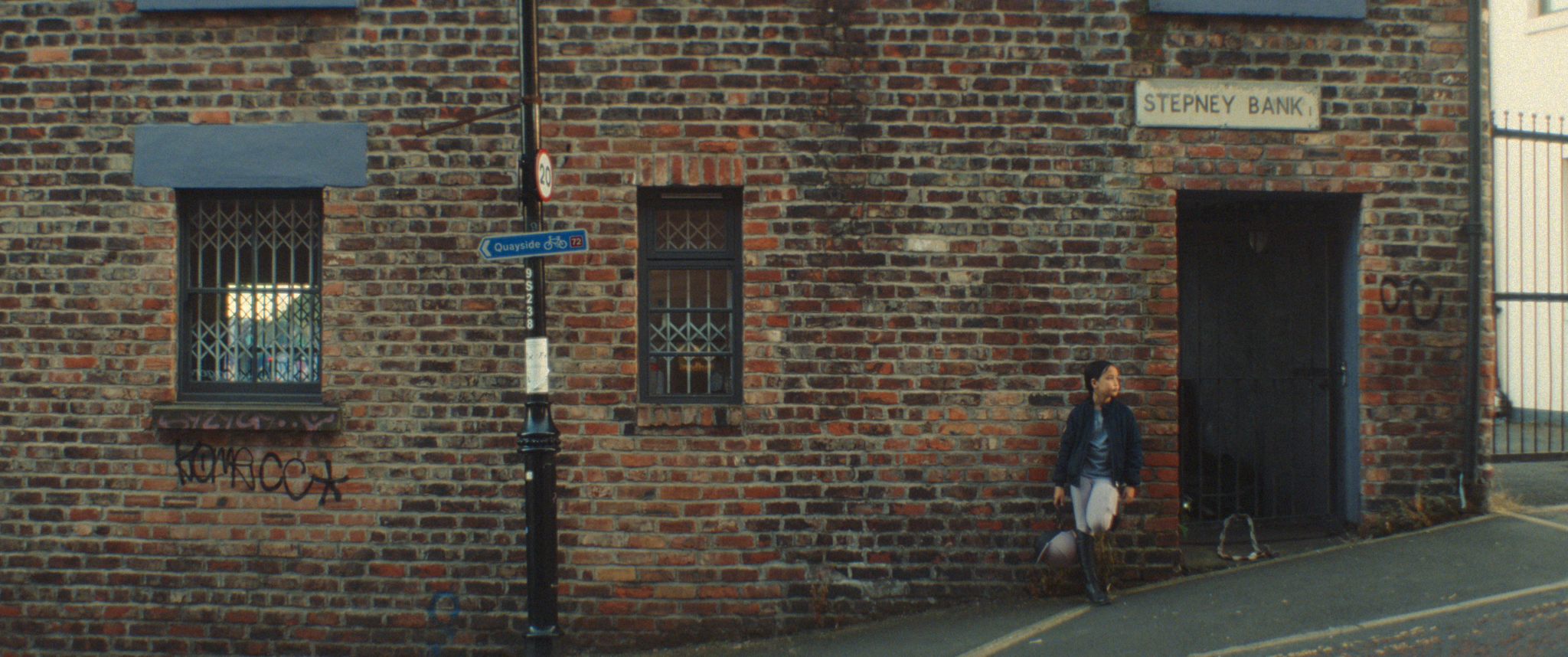 Weathered brick building with a doorway and windows, a person walking by on the pavement.