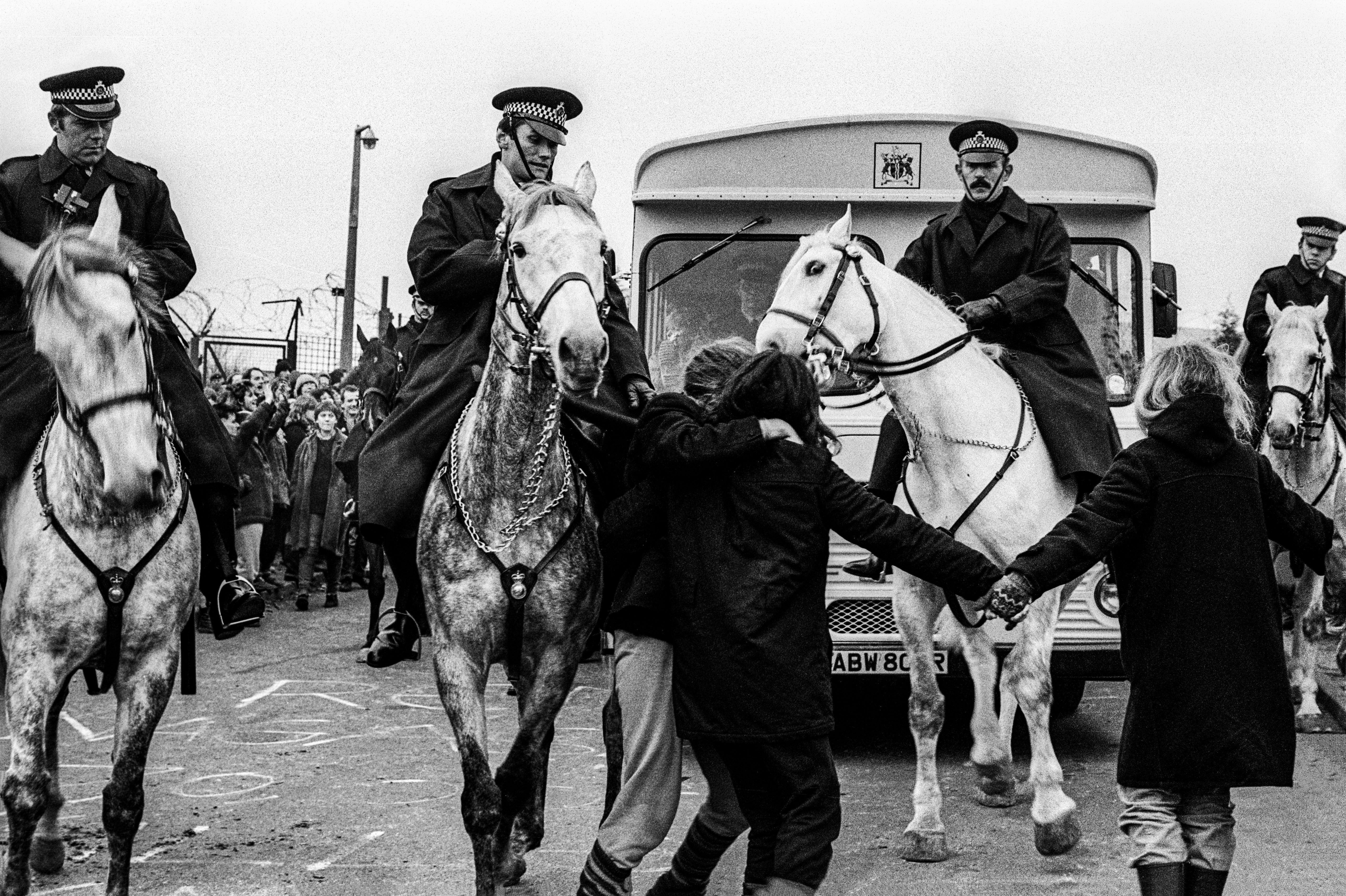 Black and white image of mounted police officers on horses with crowd and lorry in background during what appears to be a protest or civil unrest.