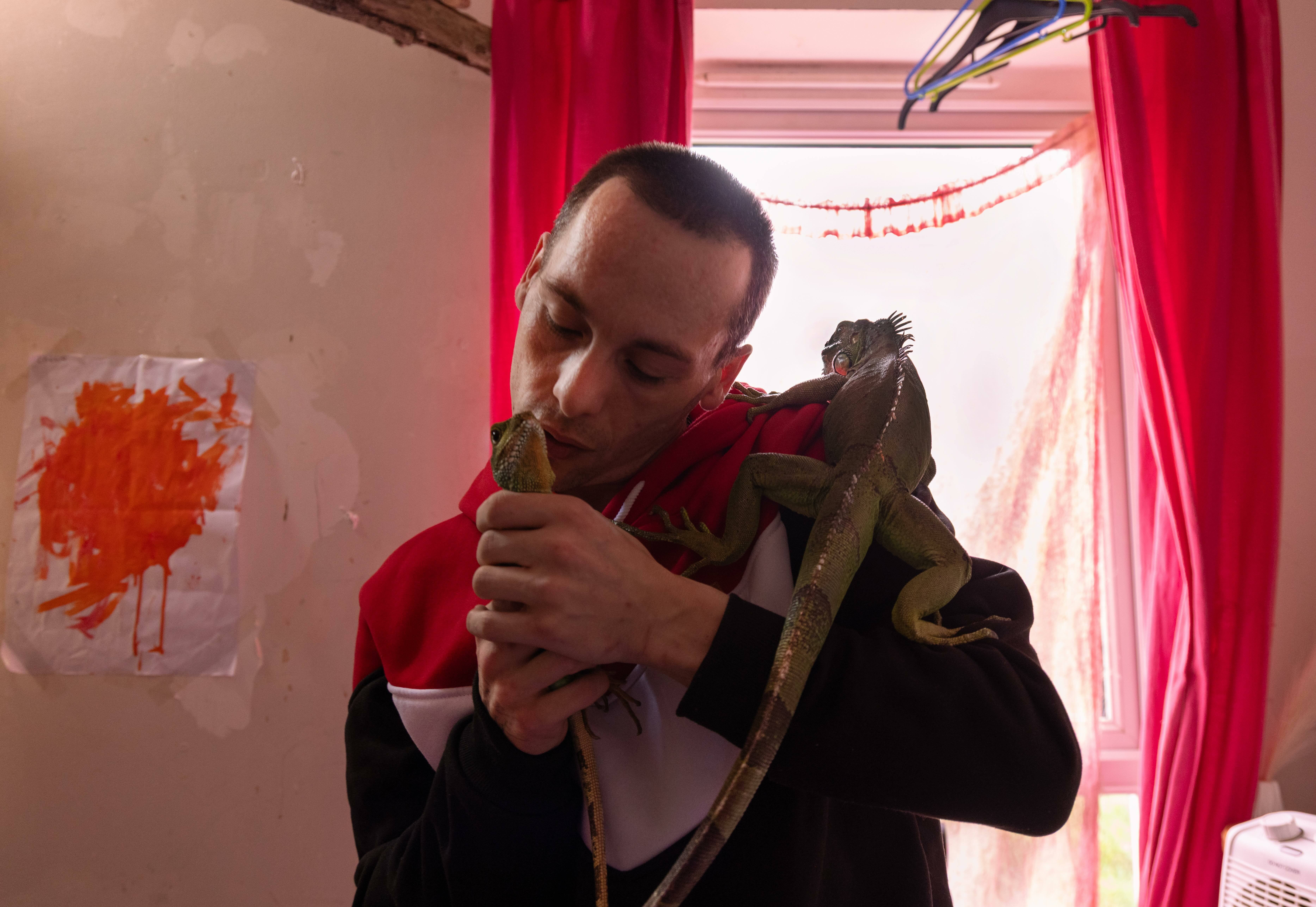 A man in a red jacket stands in a dimly lit room, holding a figurine and looking down.