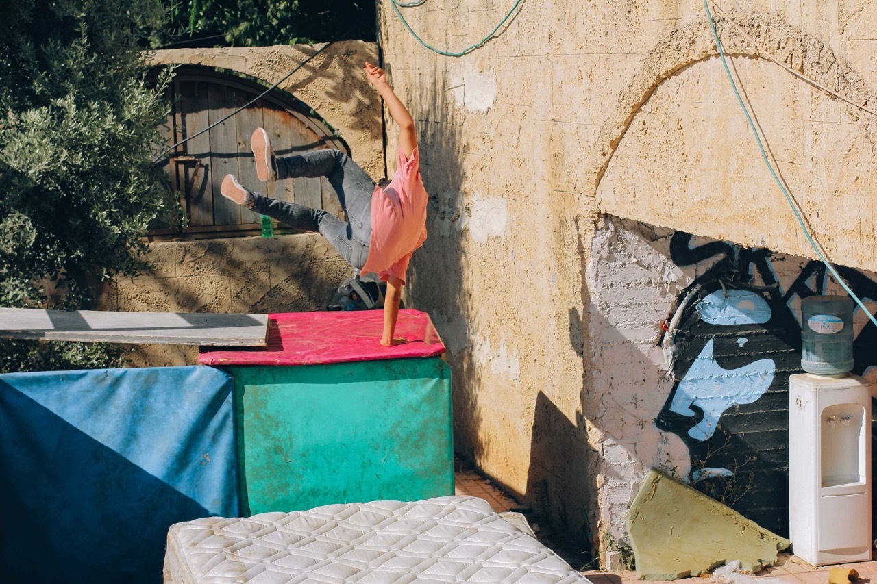 Colourful abstract sculpture of a person in a dynamic pose against a textured wall backdrop.