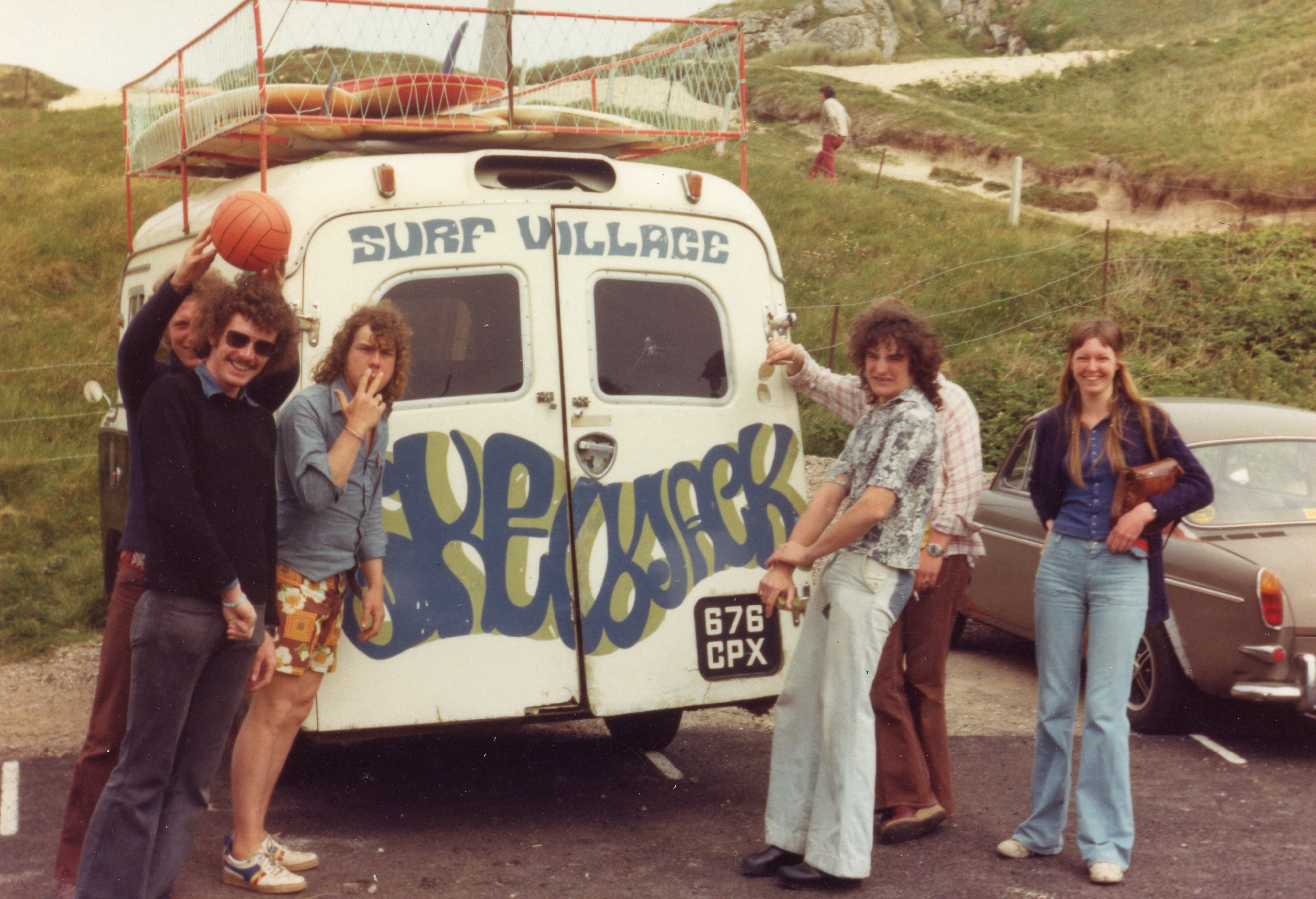A group of people standing near a vintage surf van with "Surf Village" written on the side.
