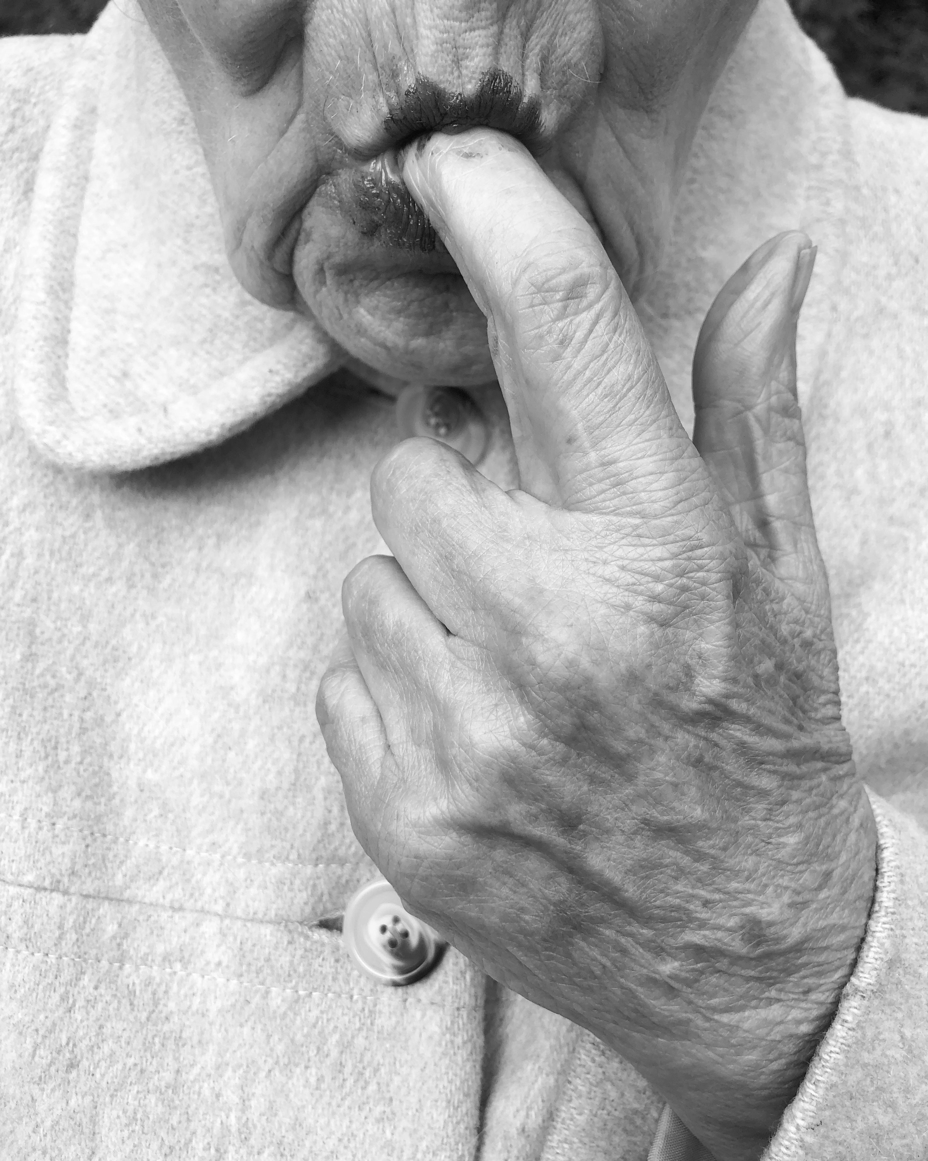 Black and white image of elderly hands with wrinkled skin and visible veins, fingers interlocked, resting on light fabric.
