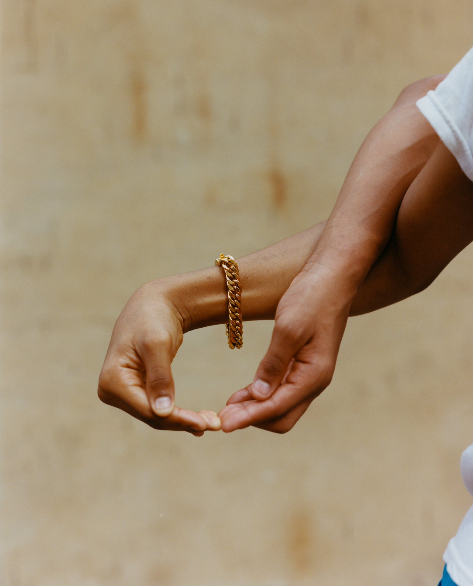 Woman's cupped hands wearing gold chain bracelet against sandy beige background.