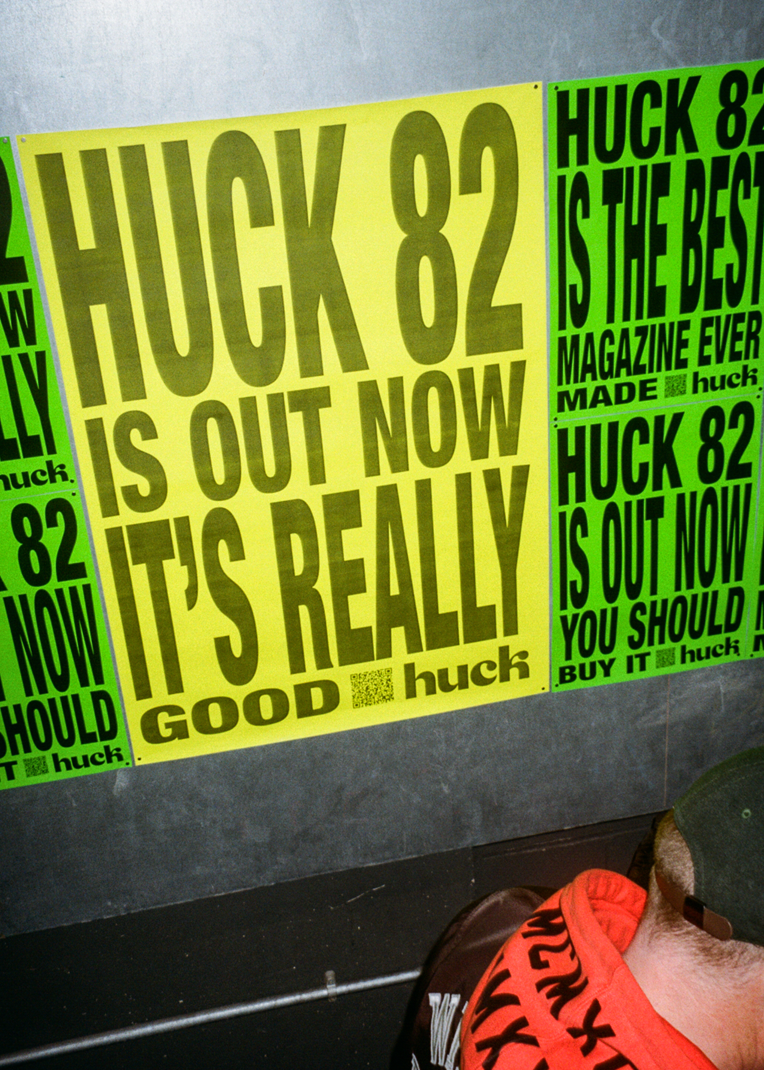 Bright yellow promotional posters on wall advertising Huck magazine issue 82 with bold black text. Person's foot in red trainers visible at bottom.