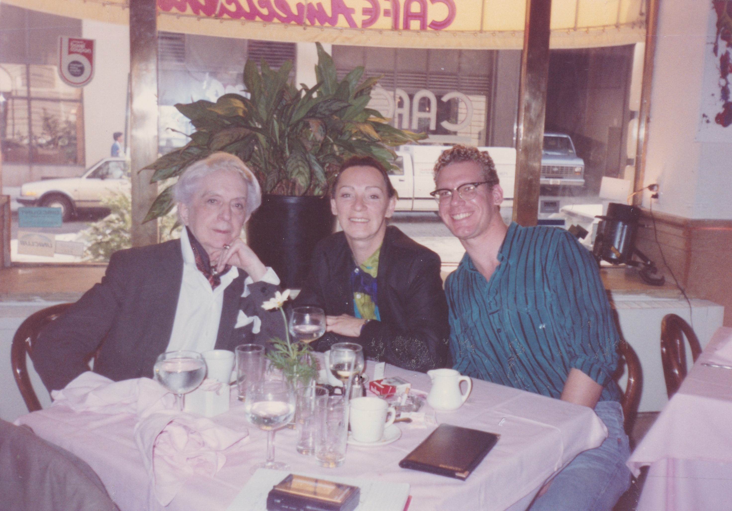 Three adults seated at a table in a restaurant, smiling and enjoying a meal together.