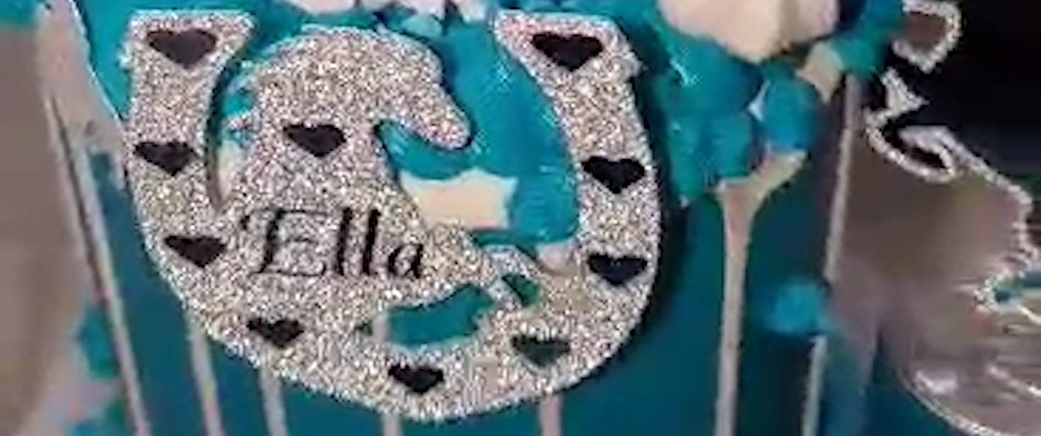 Glittery horseshoe with name "Ella" on a turquoise background, surrounded by black heart shapes.