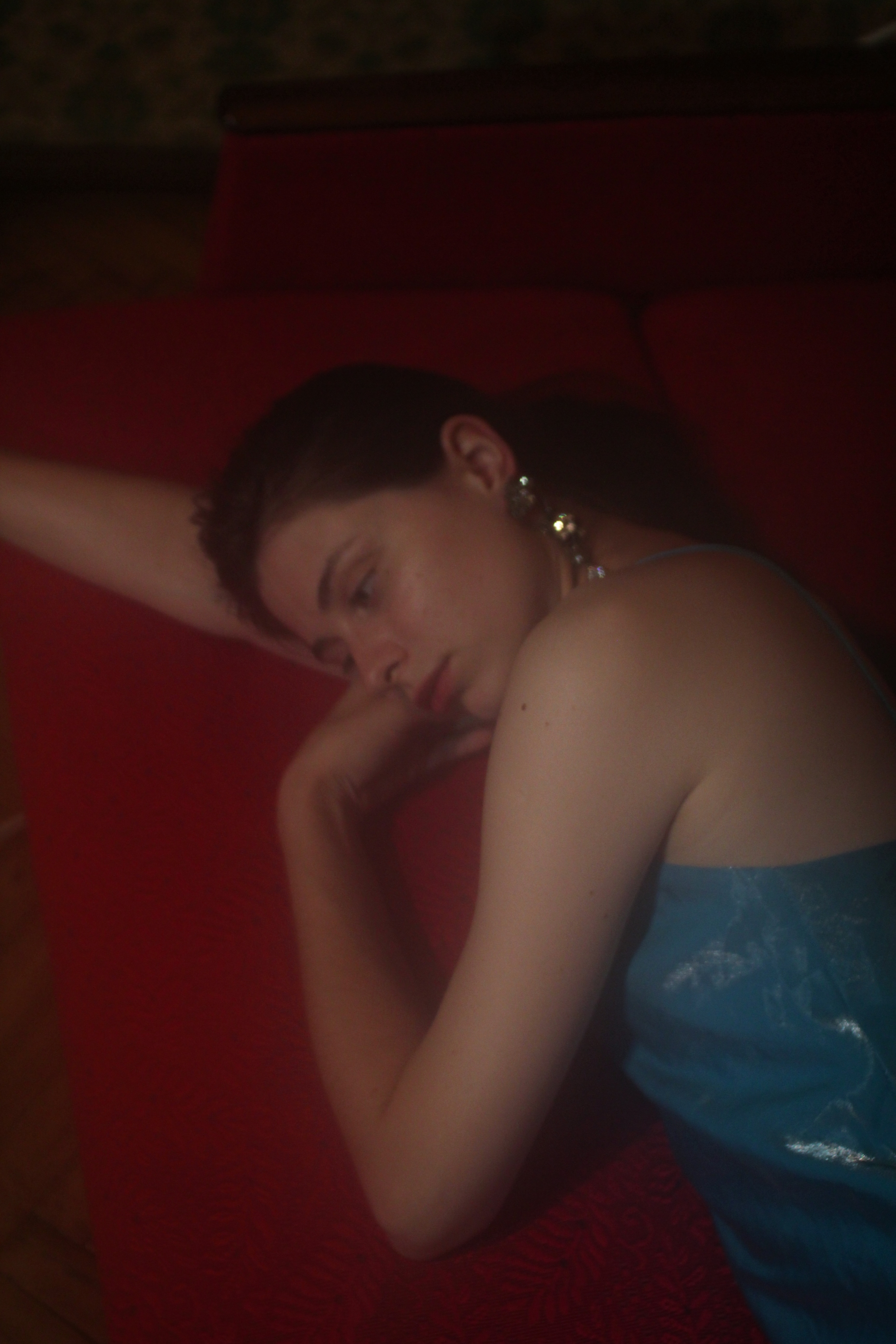 Curled figure in dark room against red and blue background.