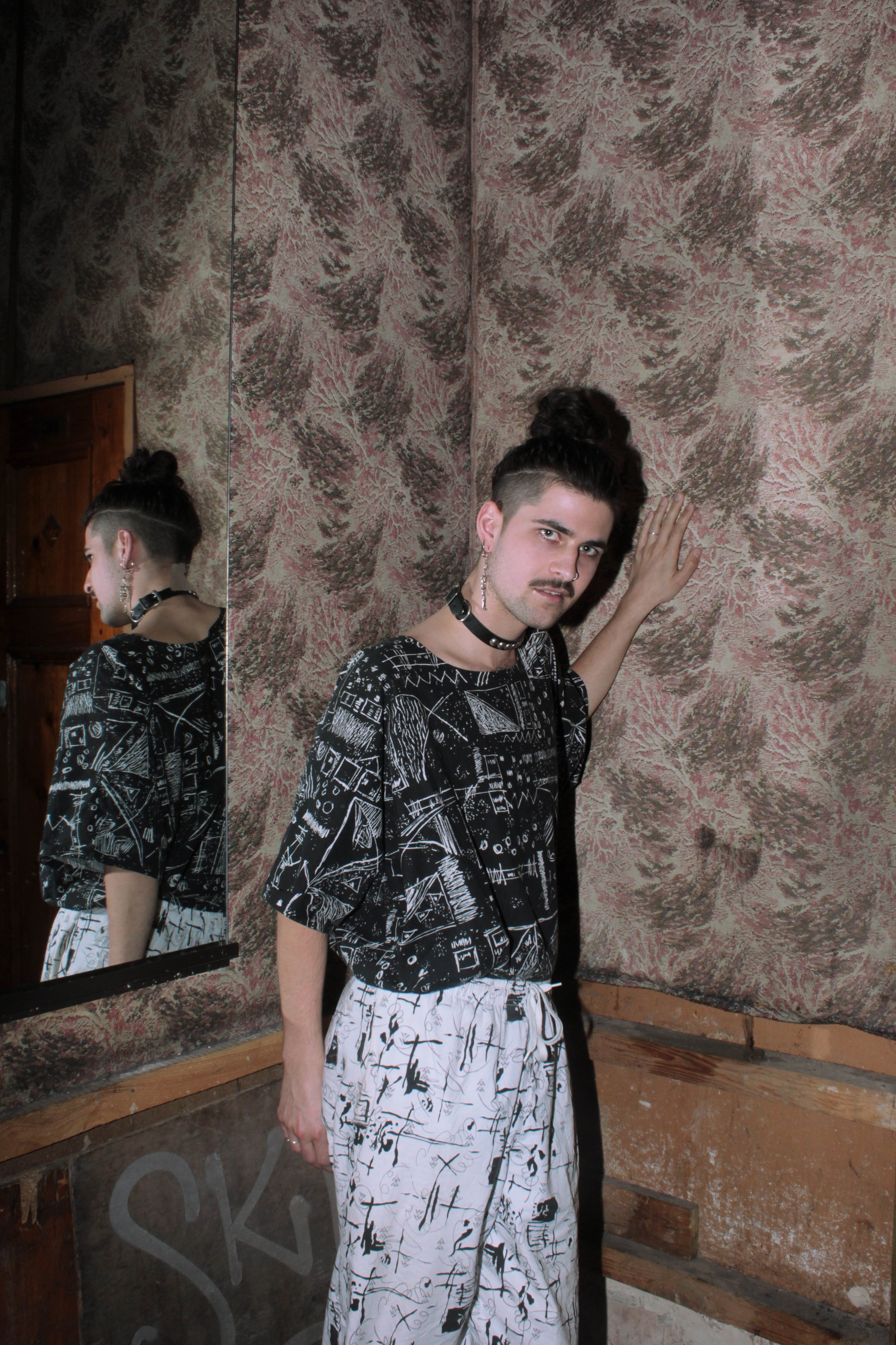 Two individuals wearing patterned clothing standing in front of a textured concrete wall.