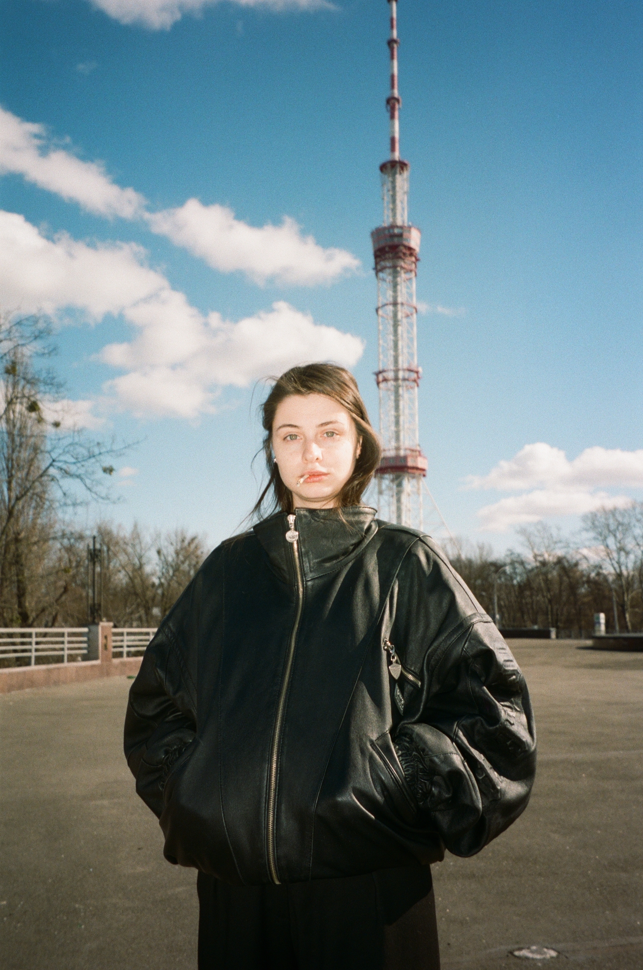 Person wearing a black jacket standing in front of a tall TV transmission tower against a cloudy sky.