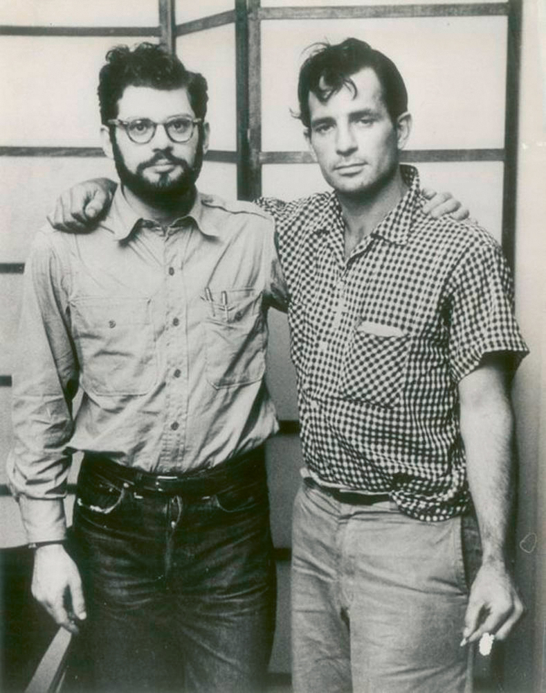 Two men in casual 1970s attire, one with a beard and glasses, the other in a checked shirt, standing together.