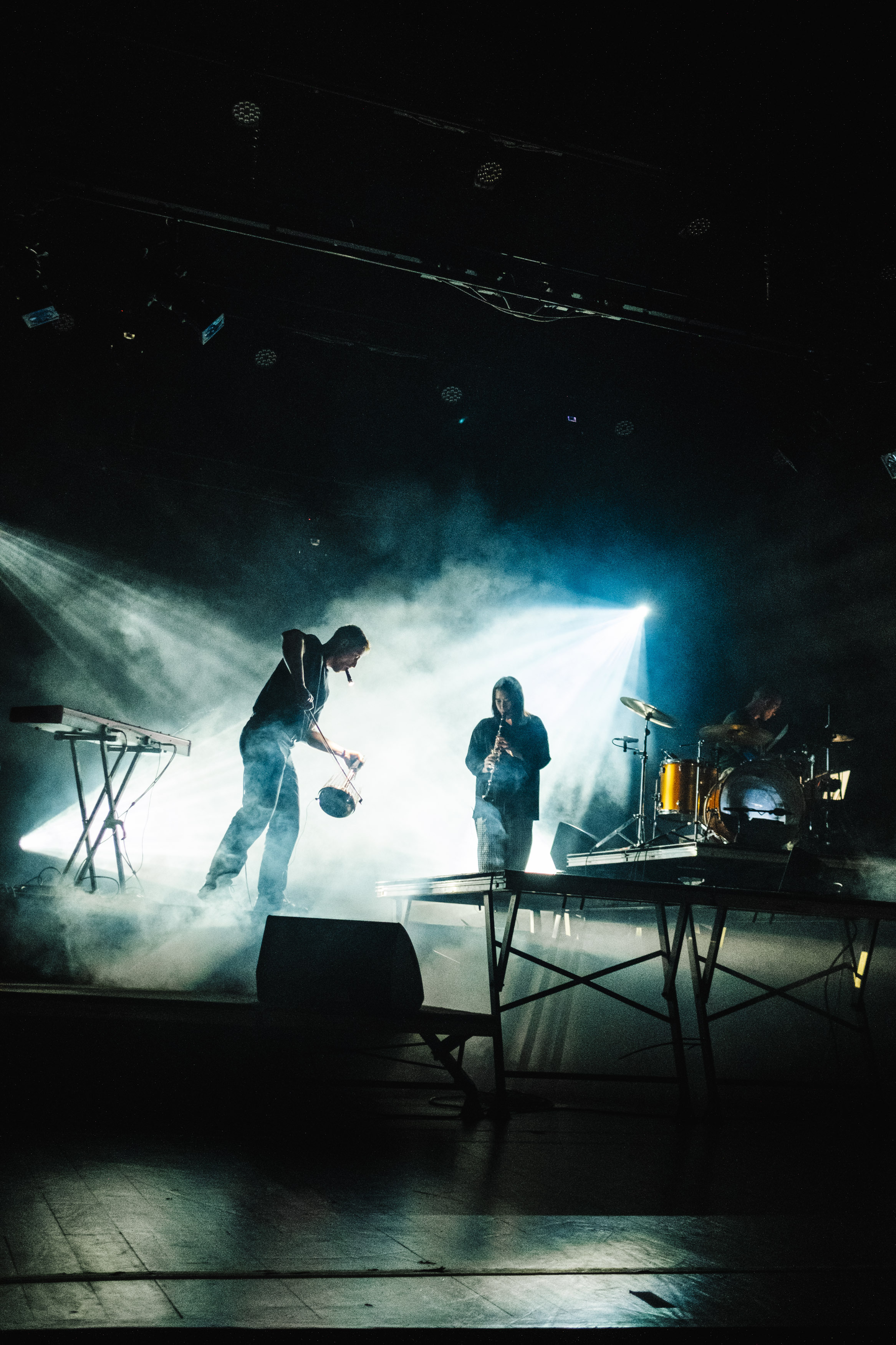 Dramatic concert stage with musicians playing in smoky, theatrical lighting.