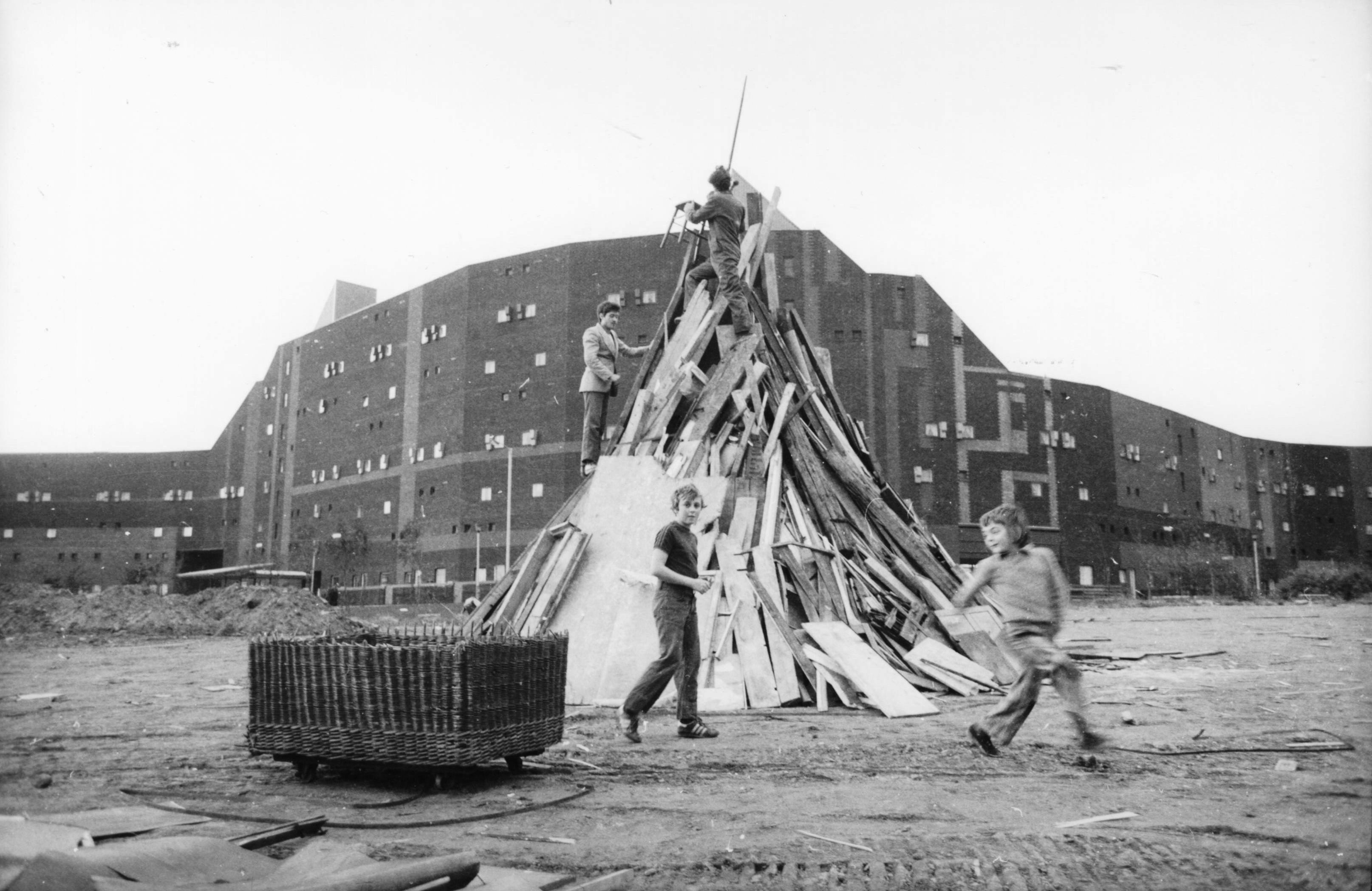 Large wooden structure amid barren landscape, figures gathered around.