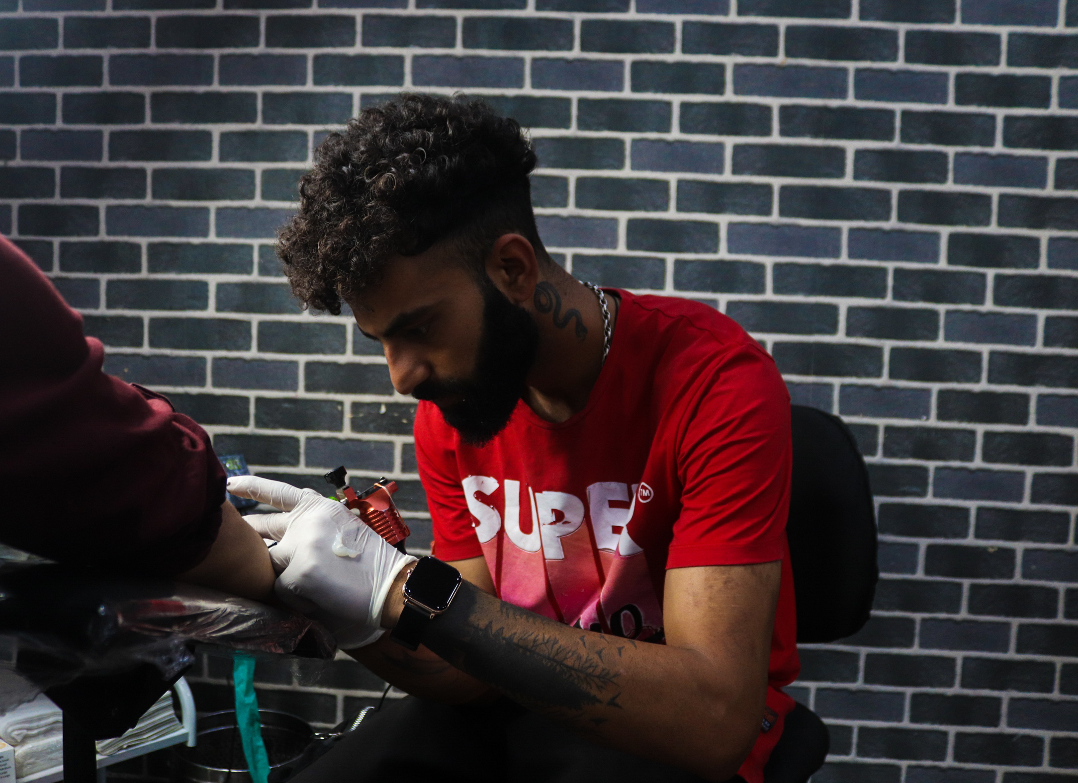 A person with curly hair wearing a red t-shirt with 'SUPER' written on it, working intently on a task.