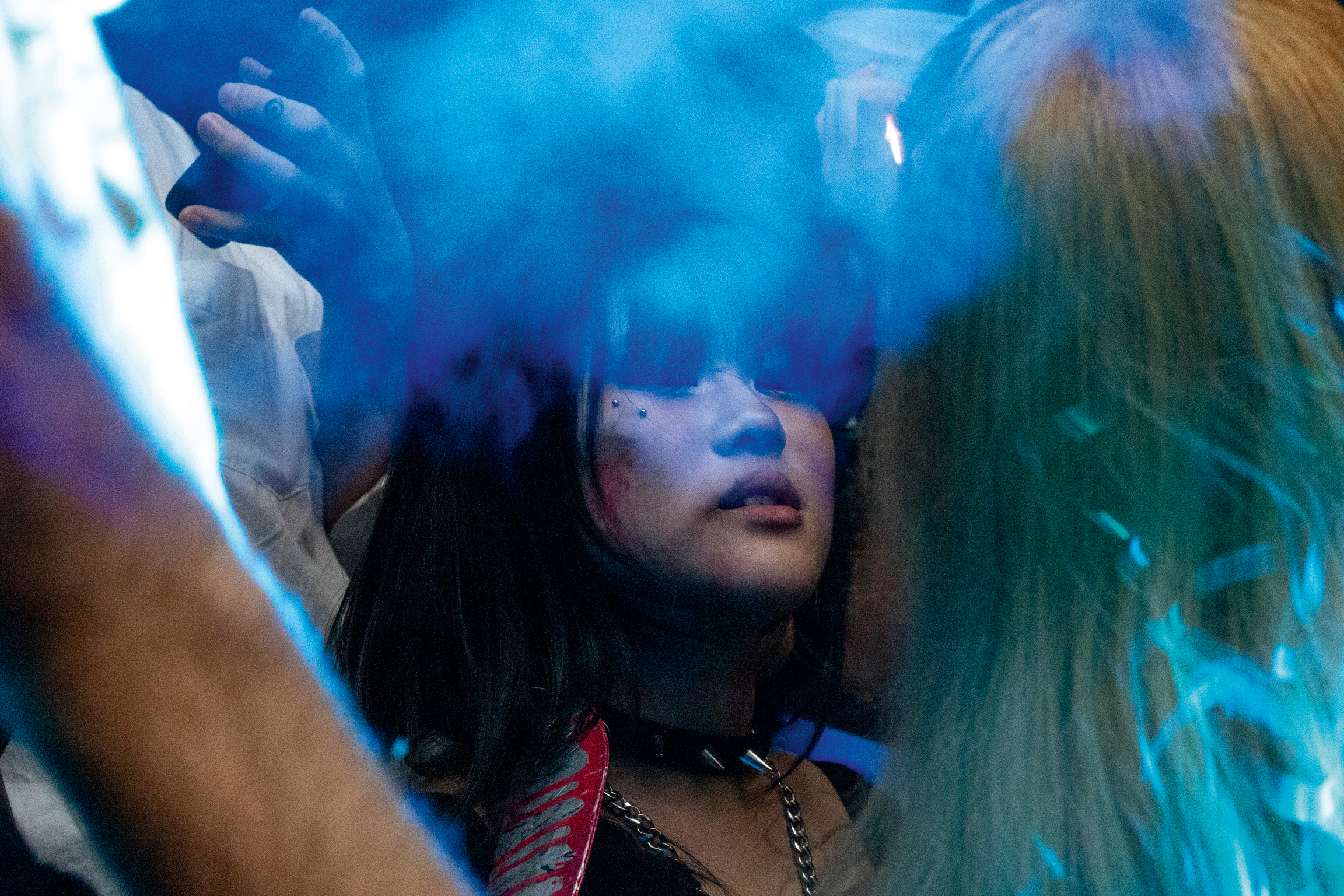 Person with dark hair surrounded by bright blue smoke or vapour, with warm light creating orange tones on edges.