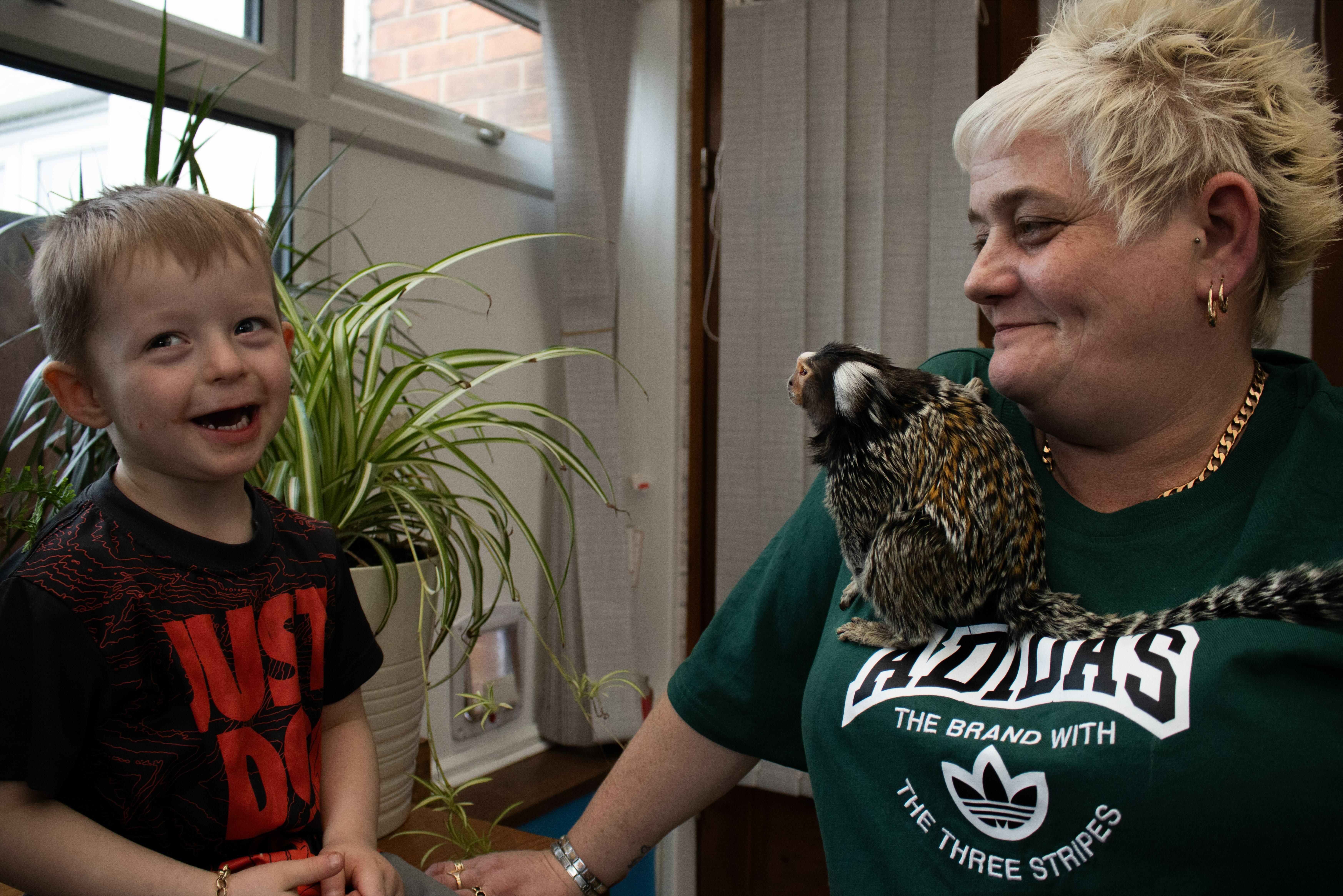 A young child and an elderly woman with short grey hair, both smiling, as the woman holds what appears to be a furry pet.