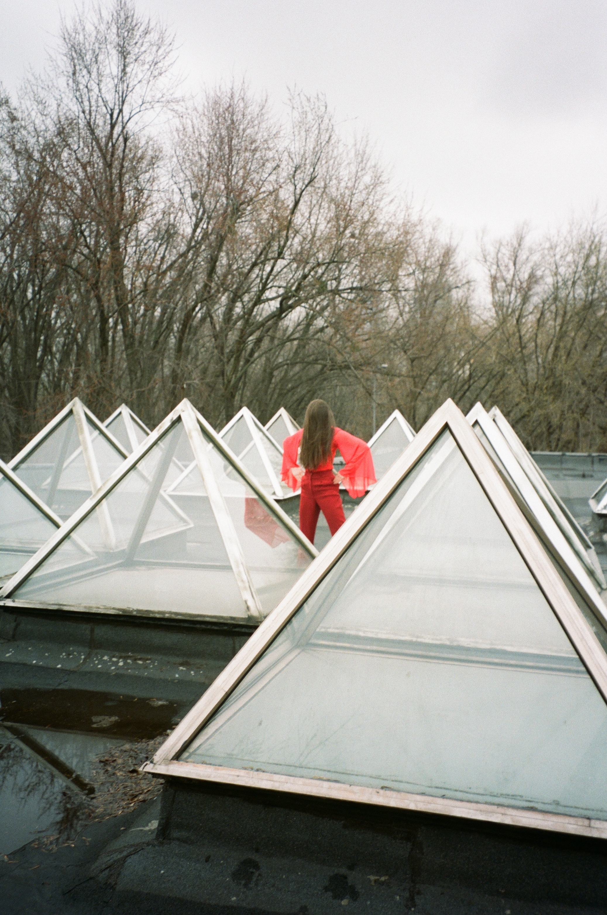 Glass pyramidal structures with a person in a red outfit standing on them, against a backdrop of bare trees.