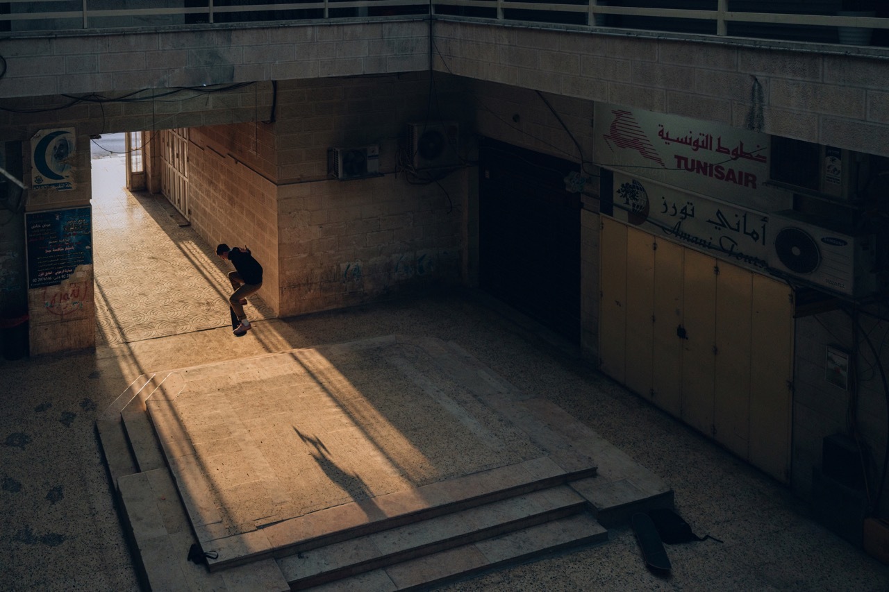 Dimly lit, derelict indoor area with wooden ramps and a lone figure in the distance.