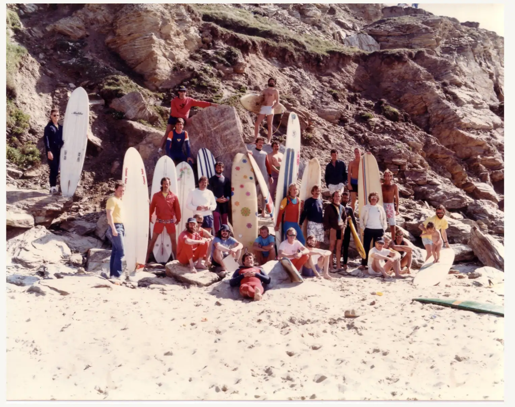 People with surfboards on a rocky beach.