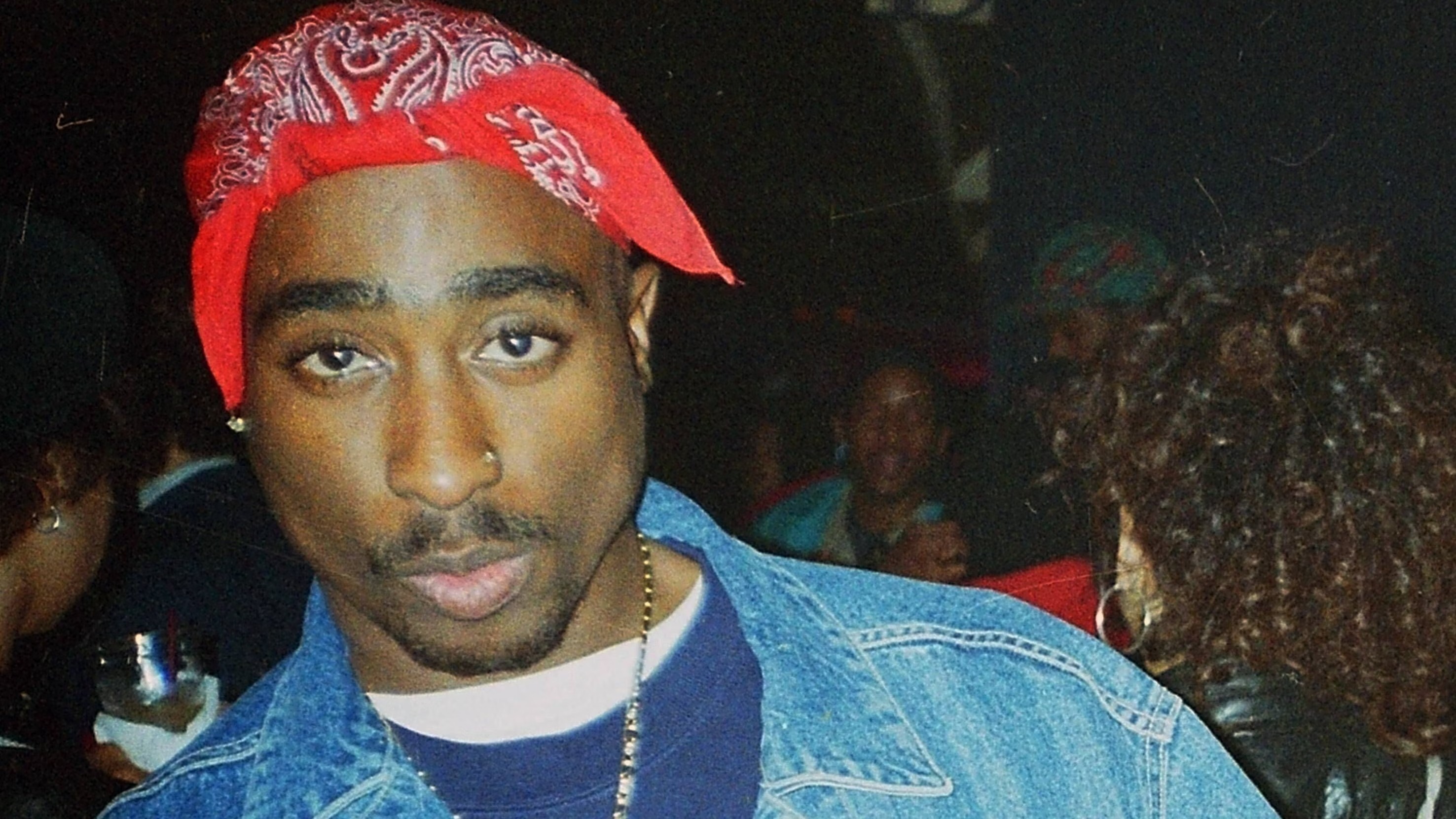 A person wearing a red bandana and denim jacket, looking directly at the camera.