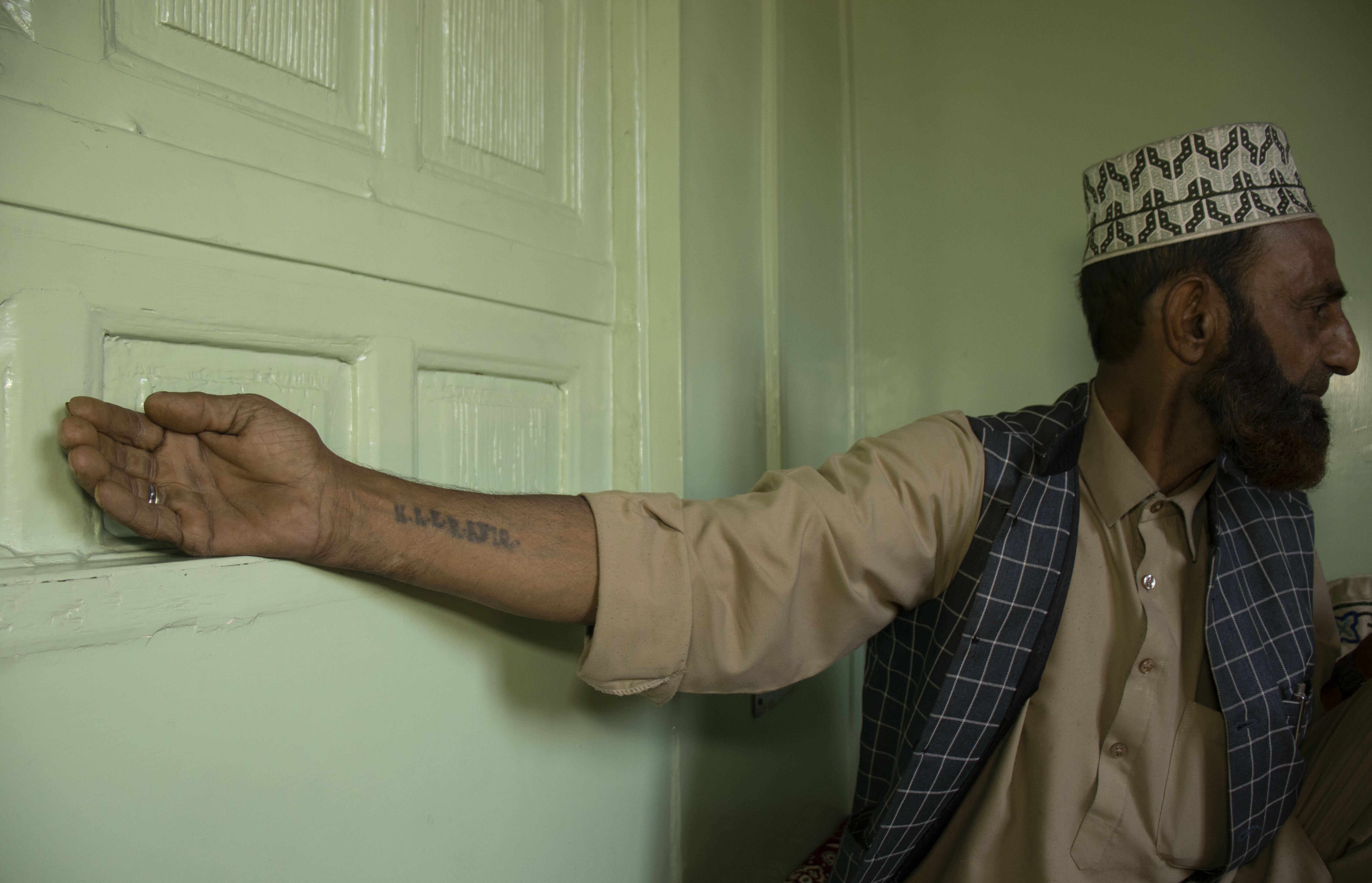 Bearded man in checkered shirt and crown, leaning on green door frame.