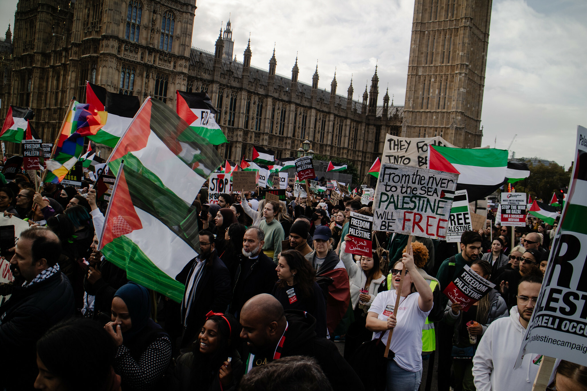 Crowd of protesters holding Palestinian flags and signs calling for "Free Palestine" outside the UK Houses of Parliament.