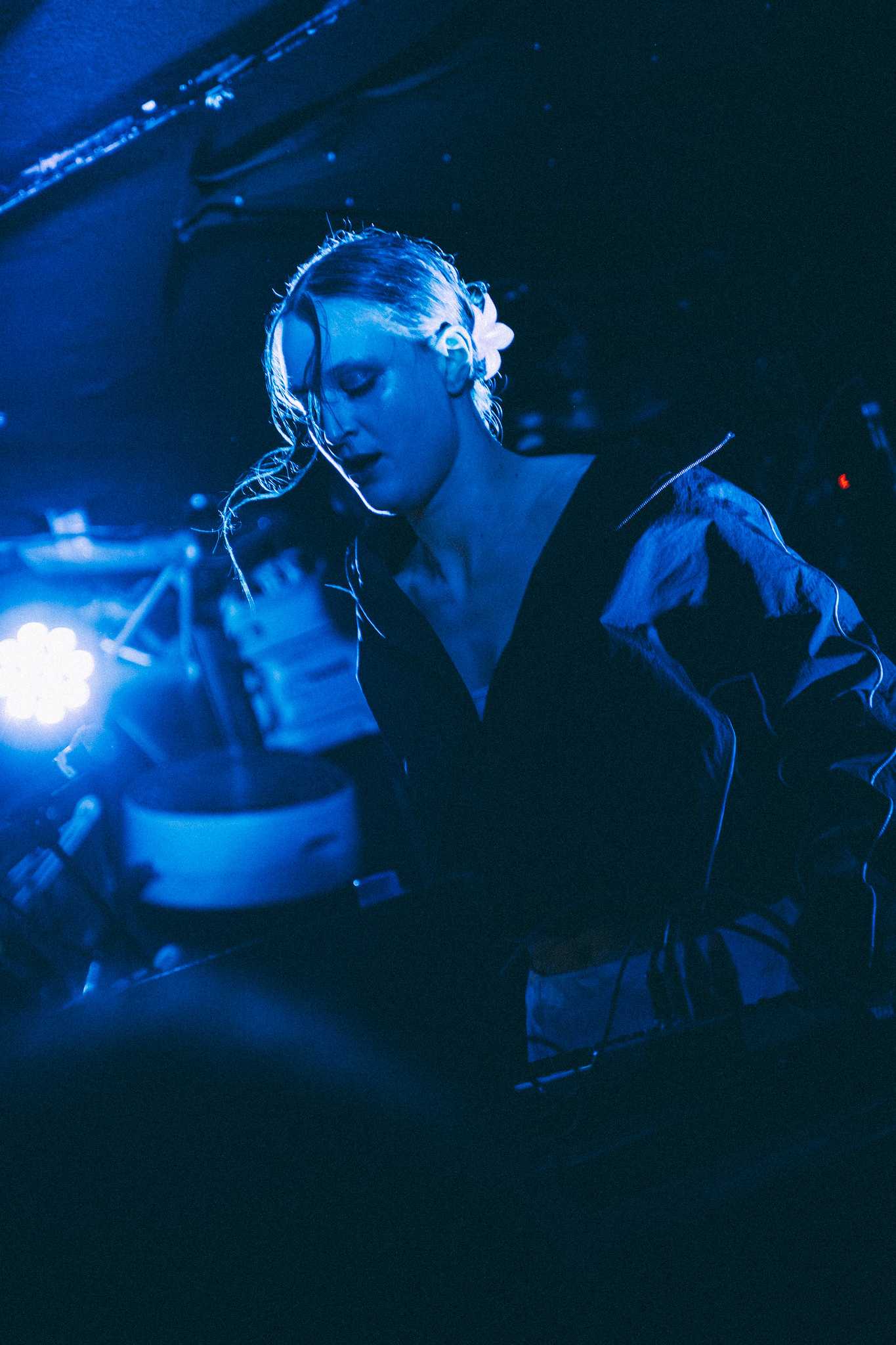 DJ wearing headphones at turntables under blue stage lighting, looking down whilst mixing music at nightclub venue.