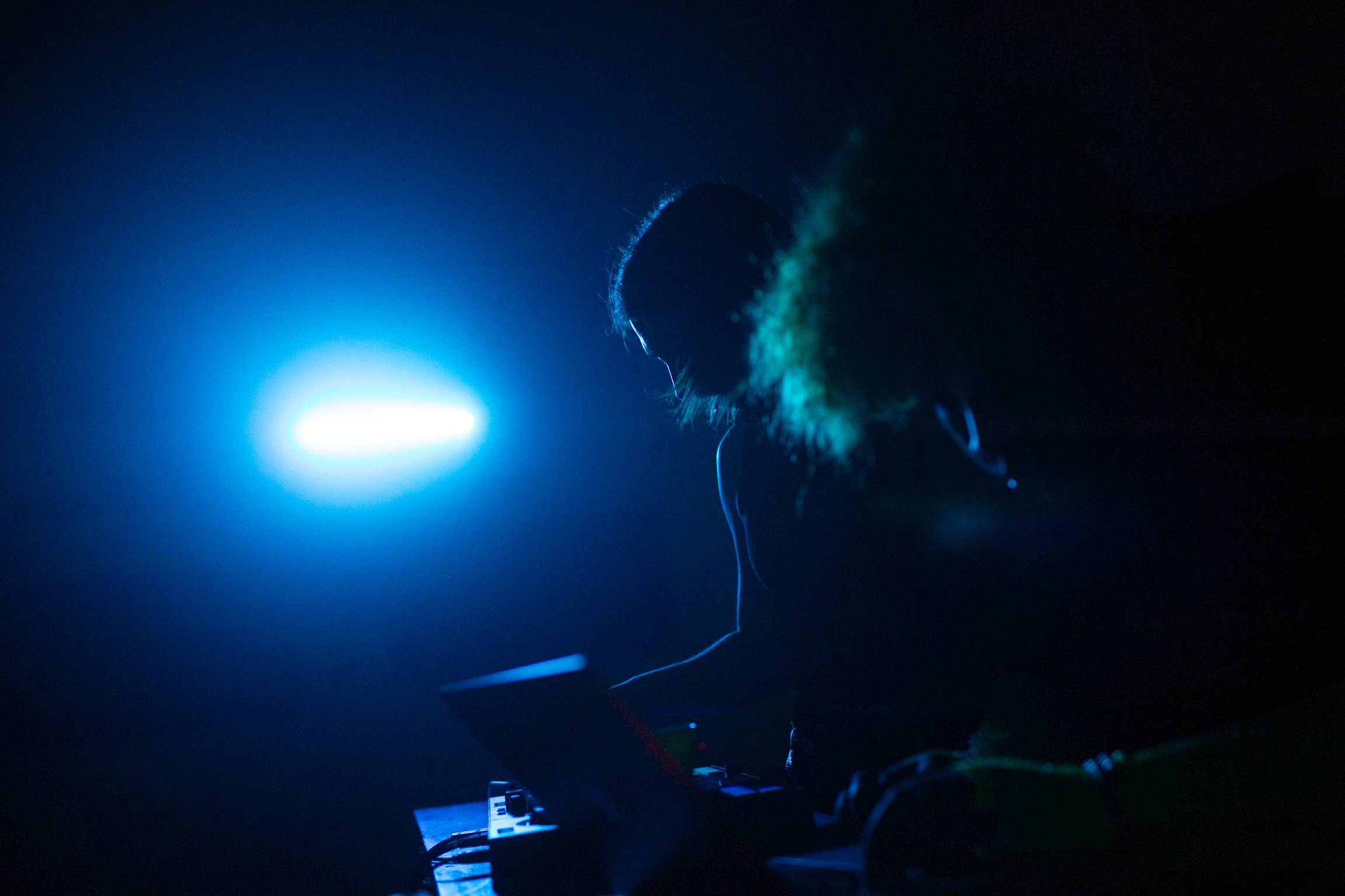Person silhouetted against bright blue light source, dark surroundings with smoke or vapour visible in blue-tinted atmosphere.