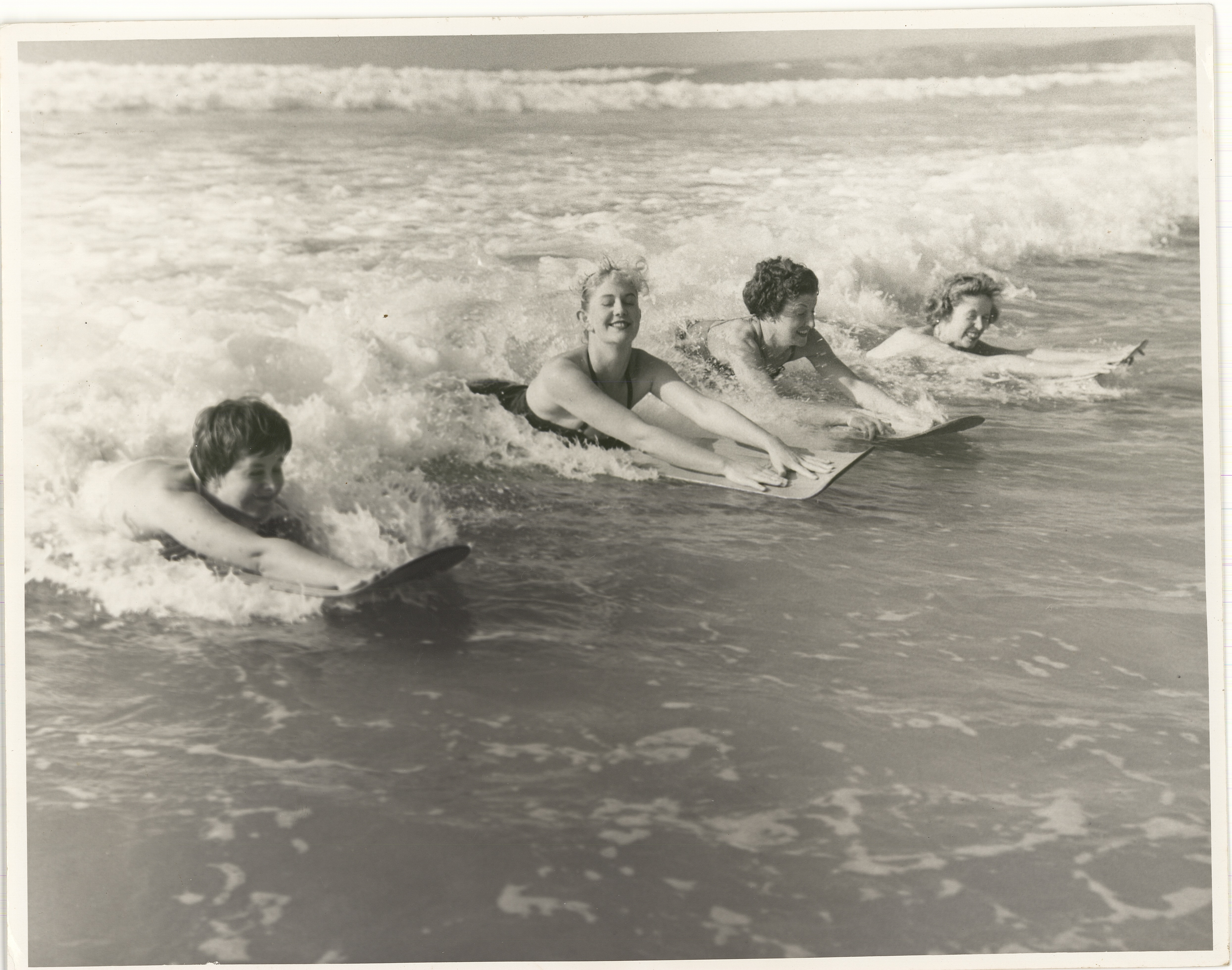 Four people surfing on waves in black and white image.