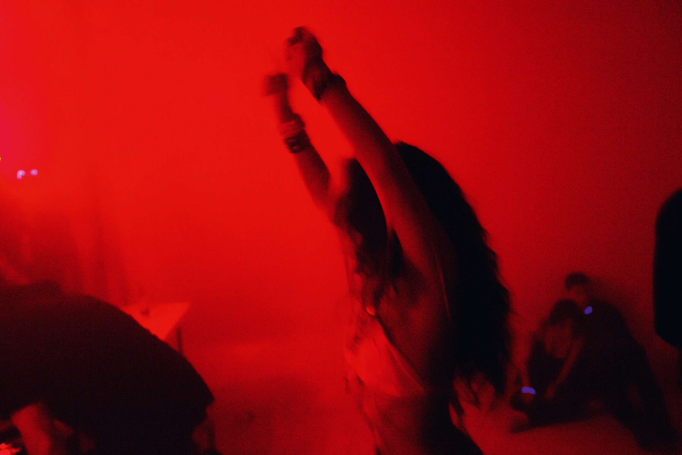 Dark silhouettes of raised hands against bright red lighting, creating high contrast between black figures and crimson background.