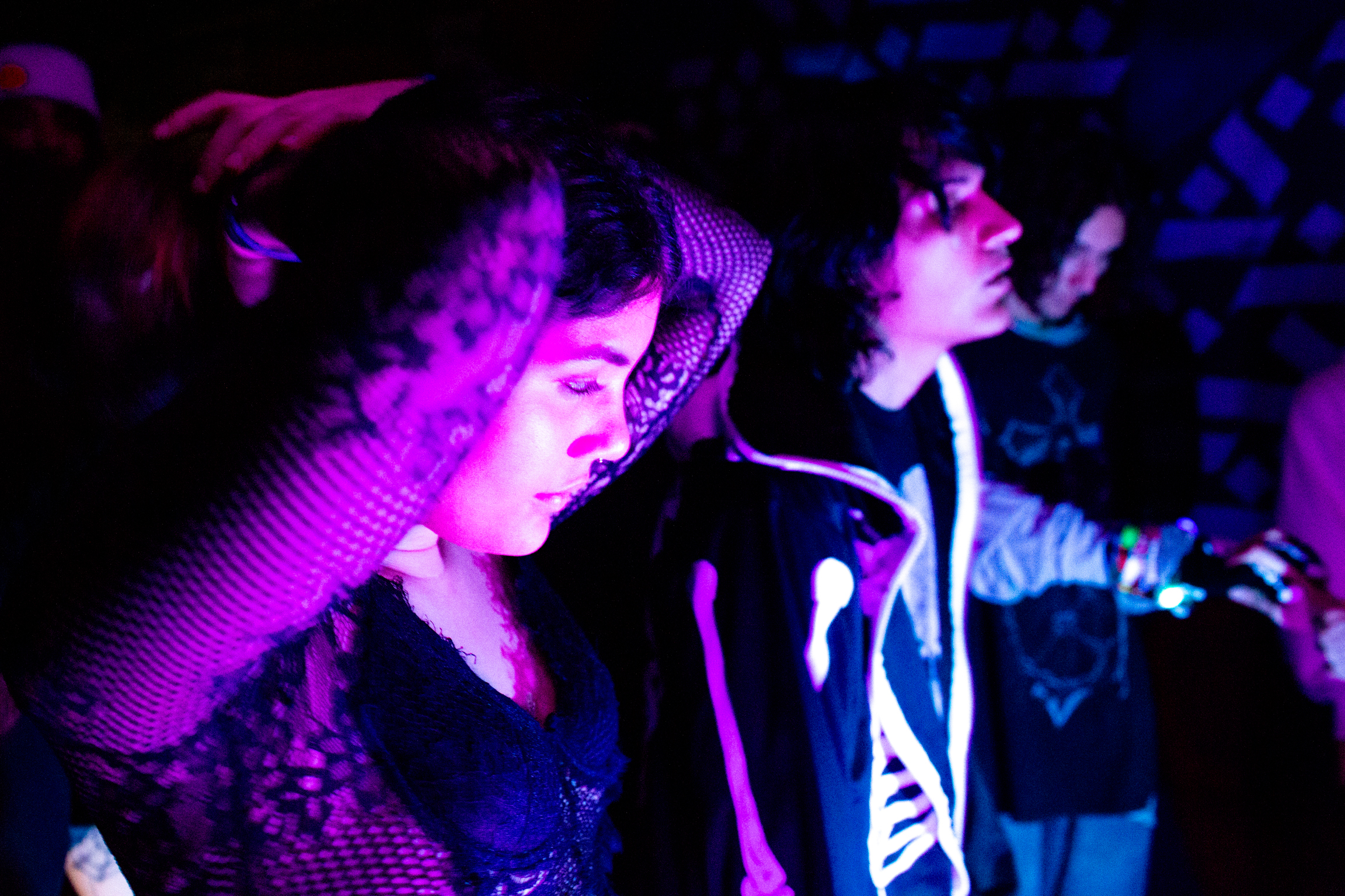 Person singing into microphone under purple and blue stage lighting, with another figure visible in background.