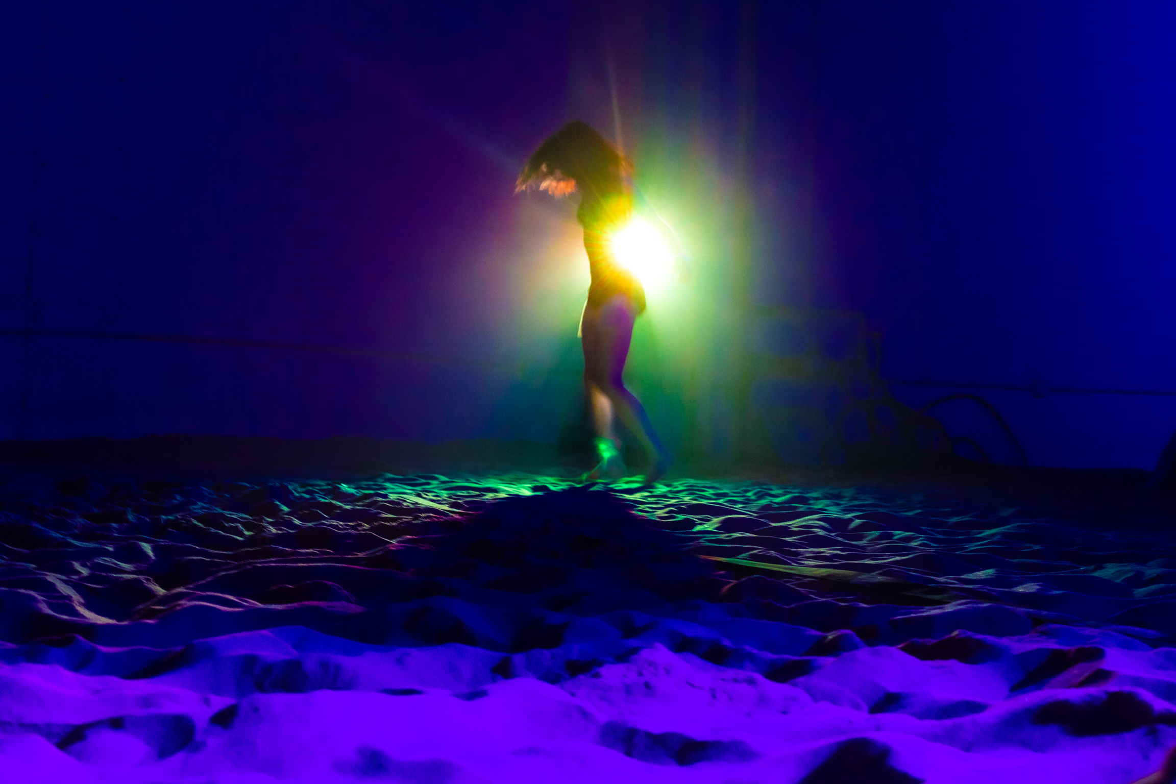 Silhouetted figure stands on snowy terrain against bright yellow-green light with blue-purple background and foreground.