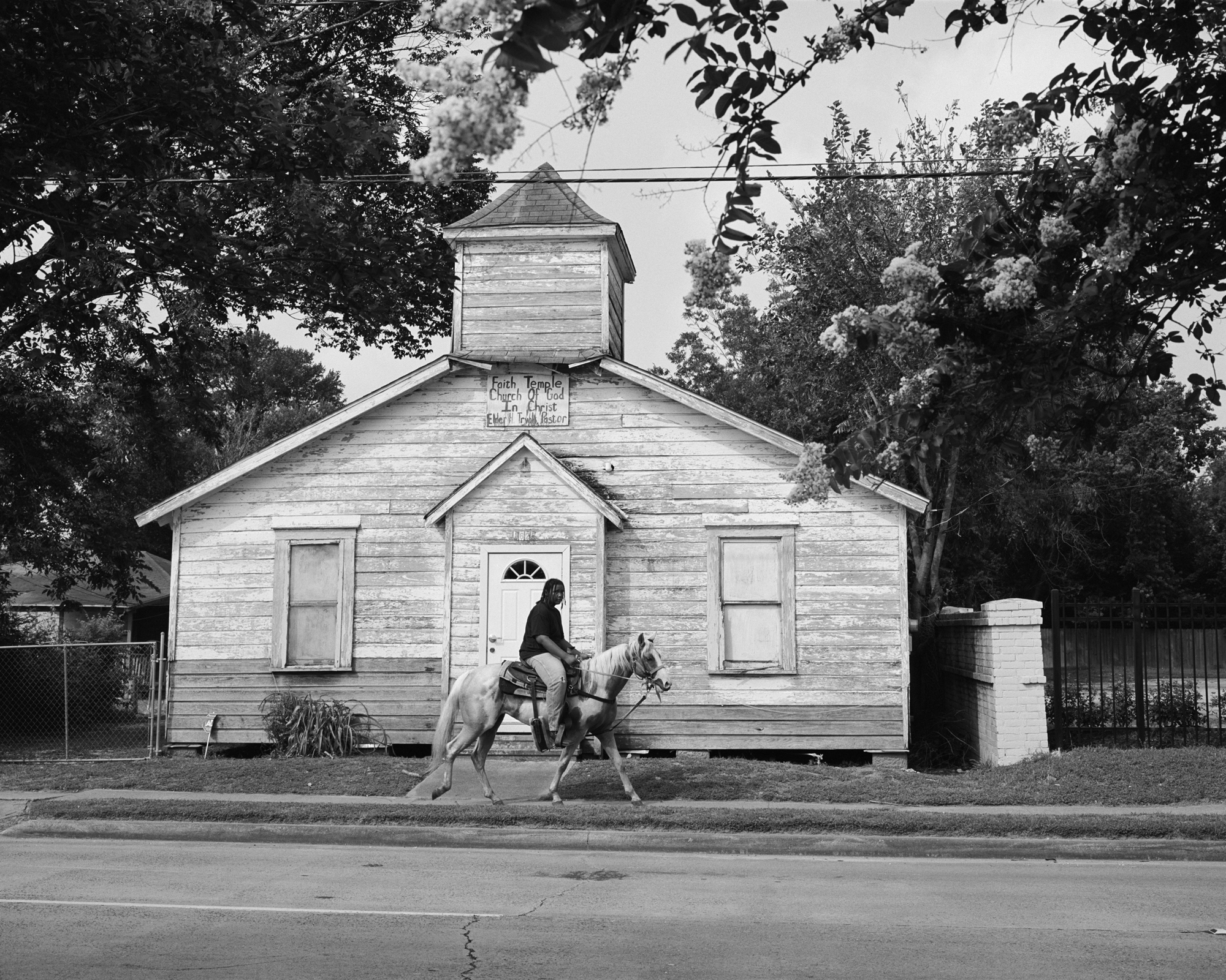 Weathered wooden building with a tall spire, person on horseback in foreground.