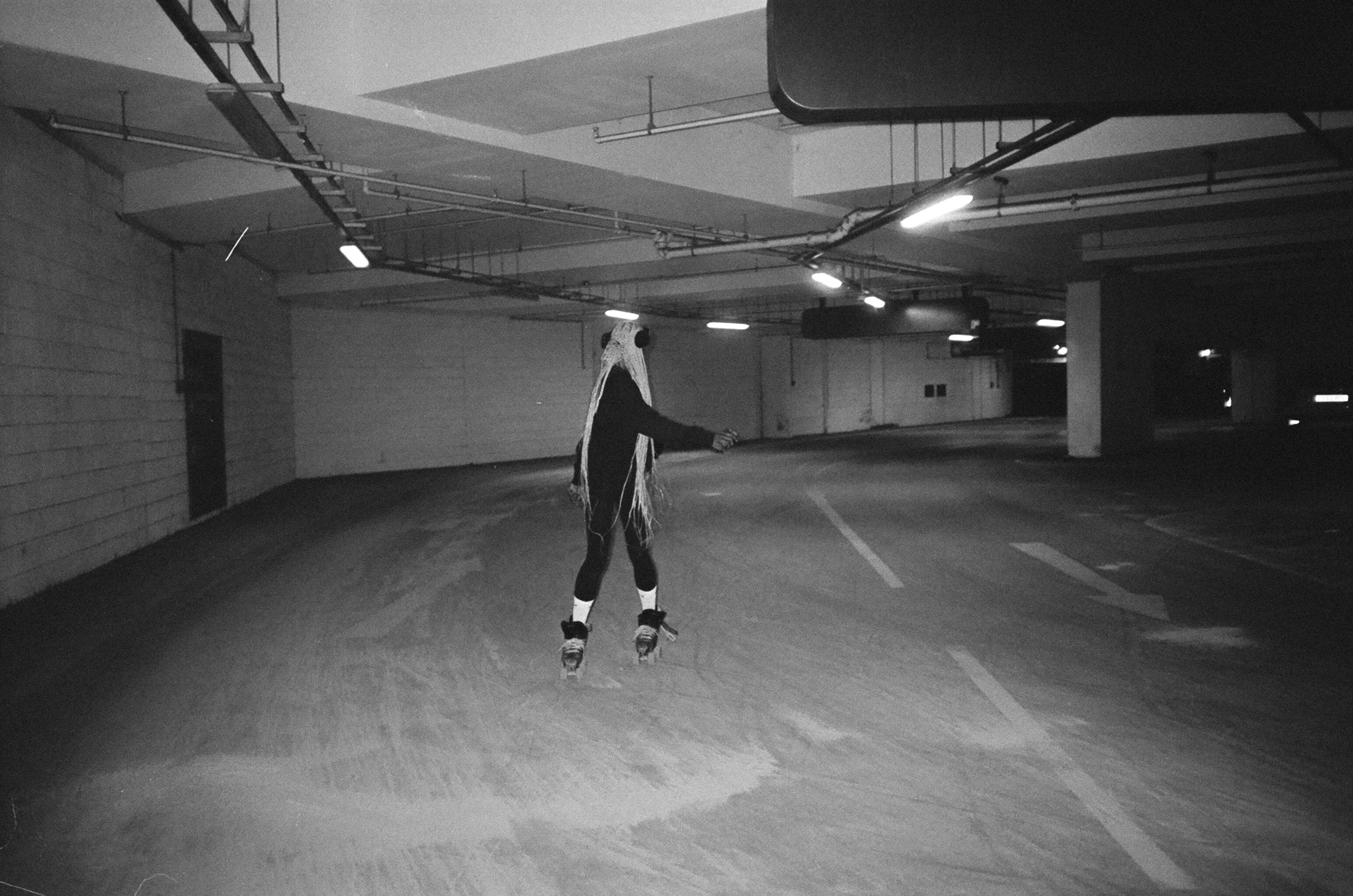 Person on roller skates in empty underground car park with concrete columns and fluorescent lighting, black and white image.