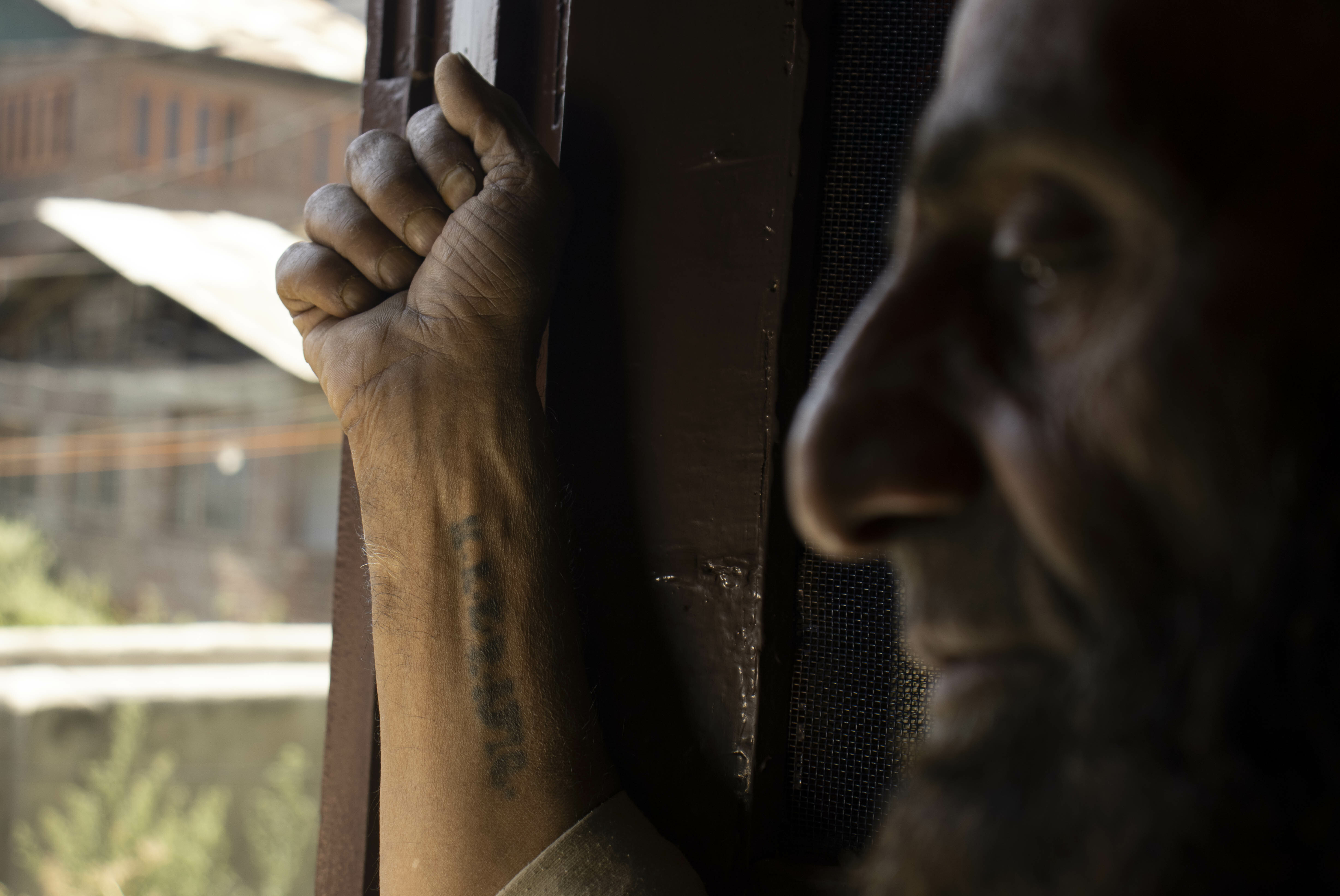 Hands grasping wooden post, person's face partially obscured in shadow.