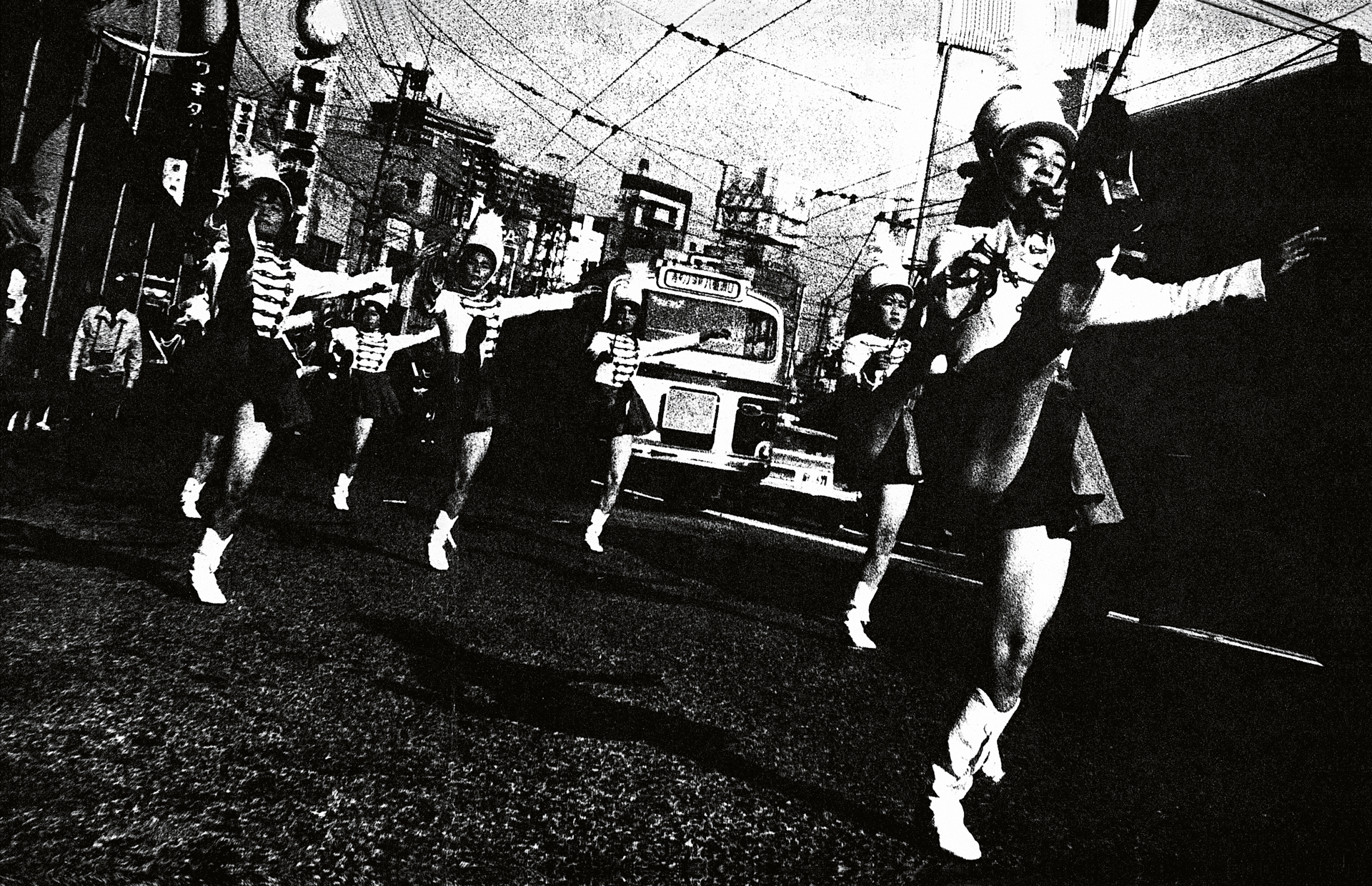 High-contrast black and white image showing people running on a street with vehicles and overhead wires. Strong shadows and grainy texture throughout composition.