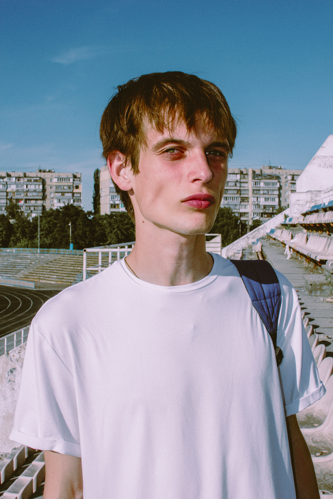 Young man in white shirt standing outdoors with city skyline in background.