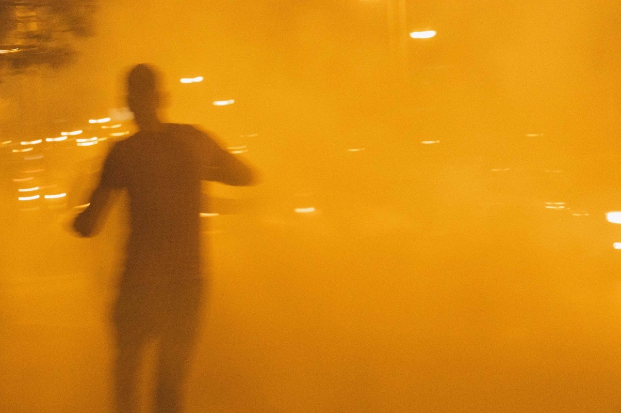 Blurred silhouette of a person moving against an orange-lit background.