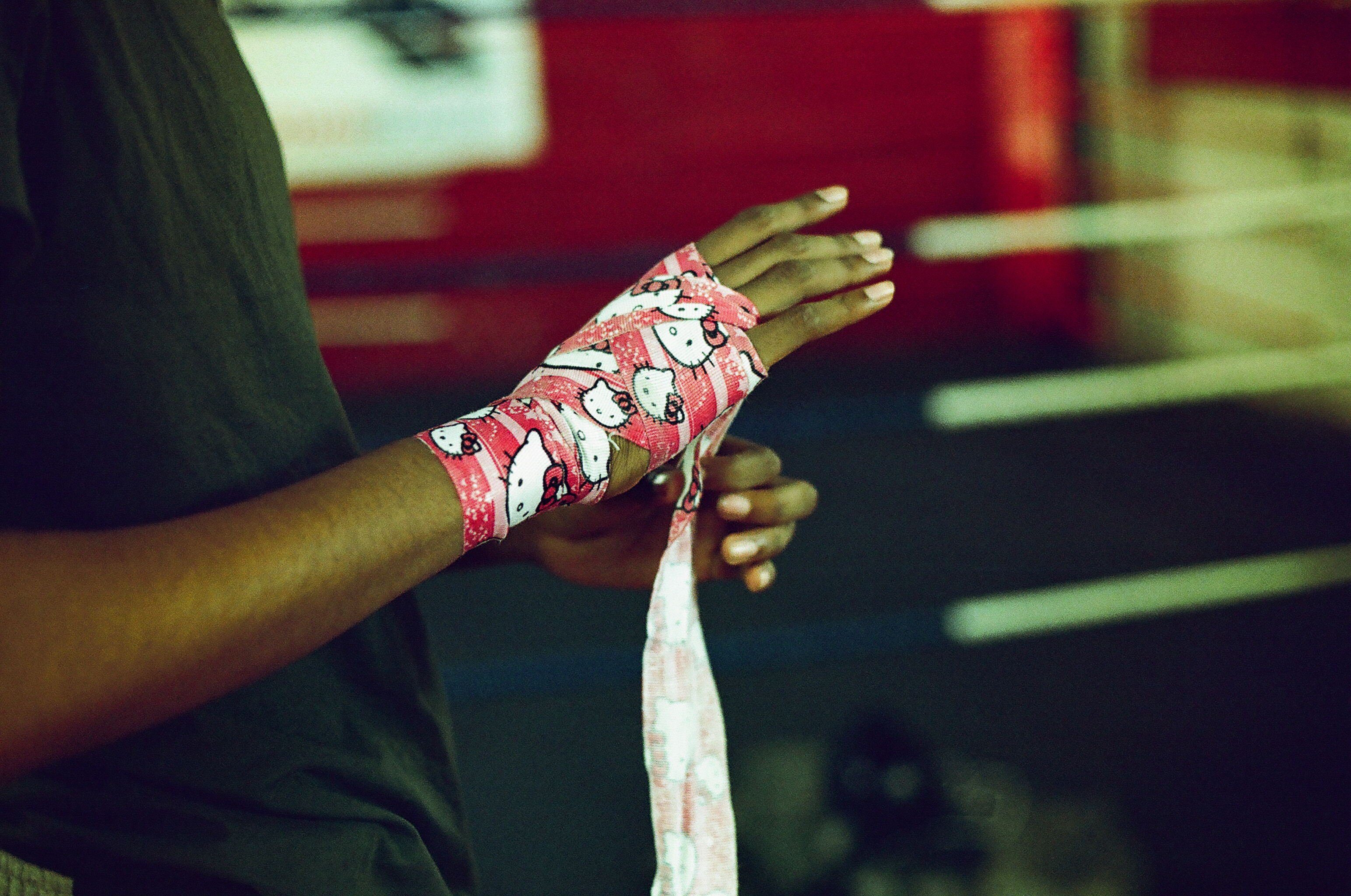 Person's hands wrapped in red and white patterned tape or bandages, with blurred red and white background.