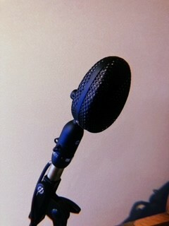 Close-up of a black microphone with a blue metallic mesh cover, set against a pink background.