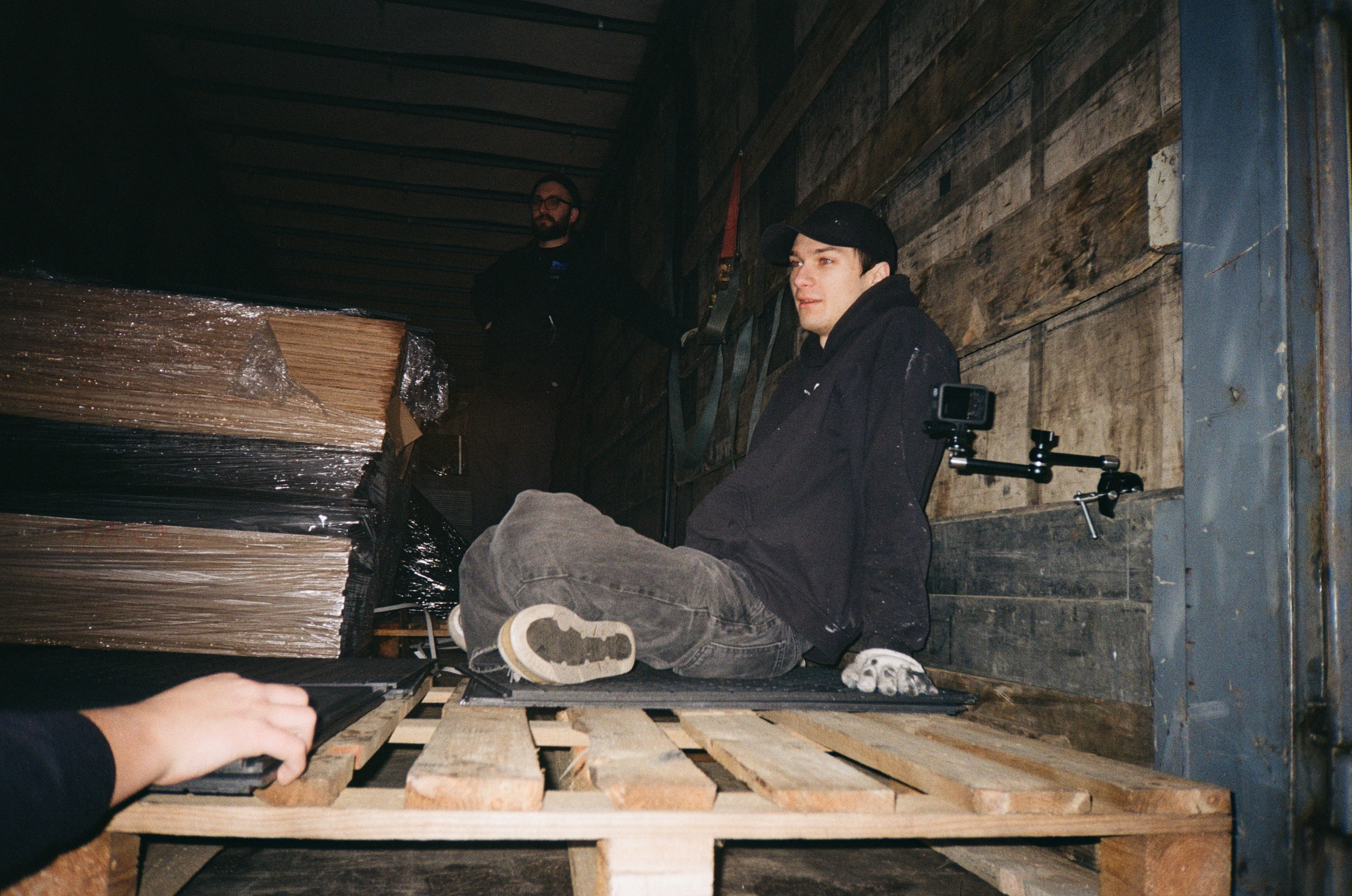 Man in black jacket working on wooden planks in dark room.