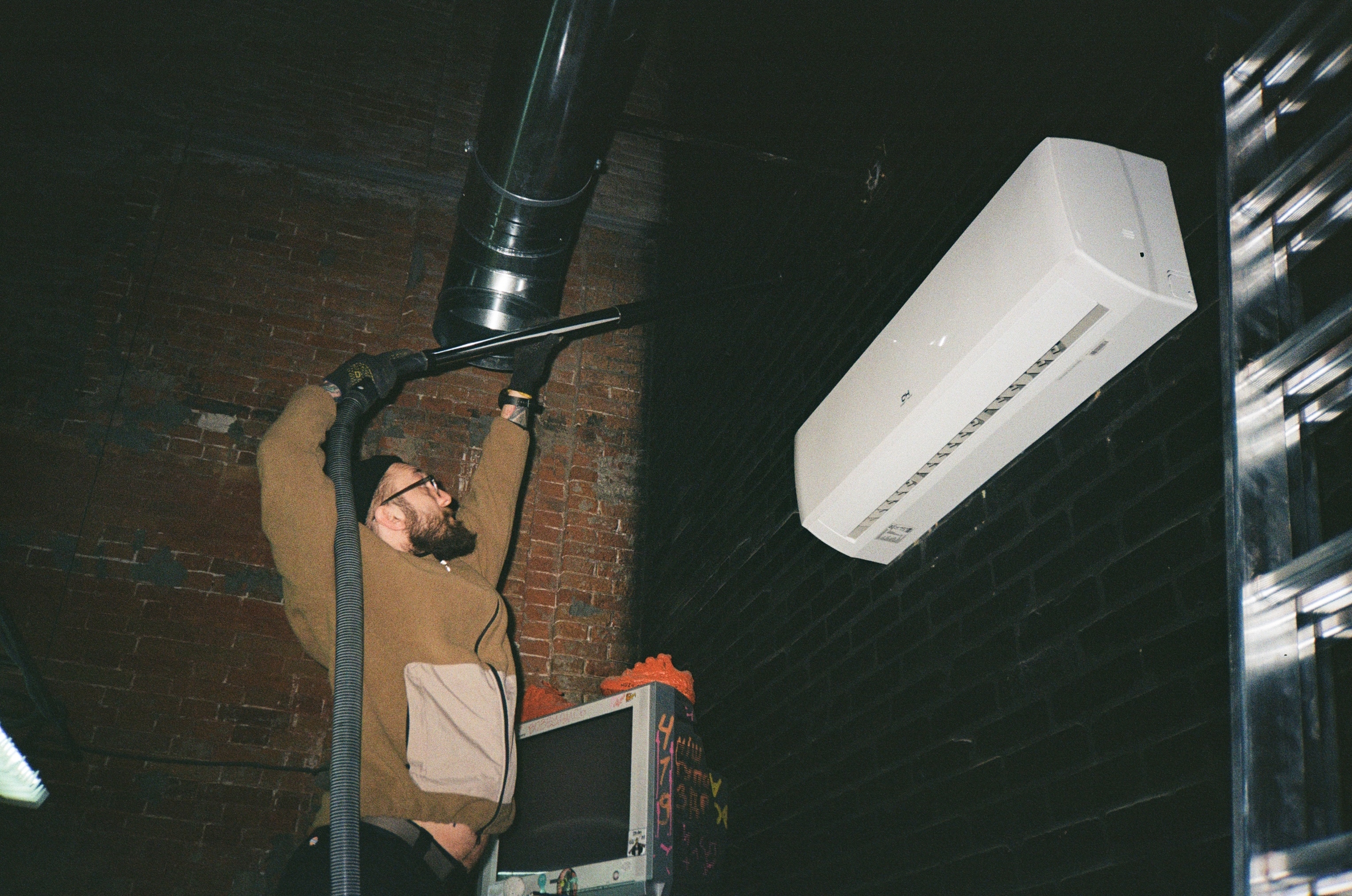 Technician repairing air conditioning unit on brick wall with toolbox
