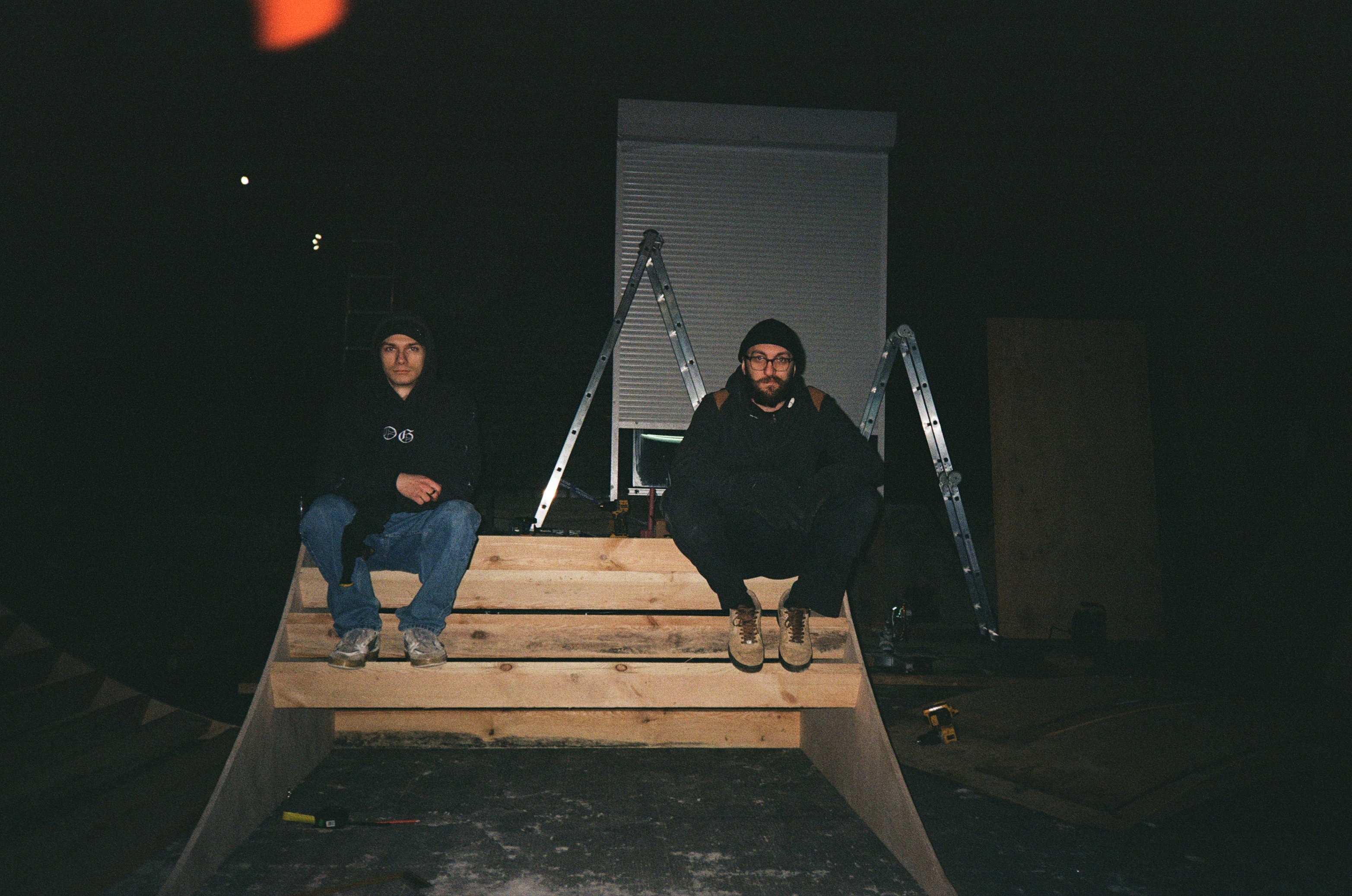 Two men sitting on a wooden structure at night.