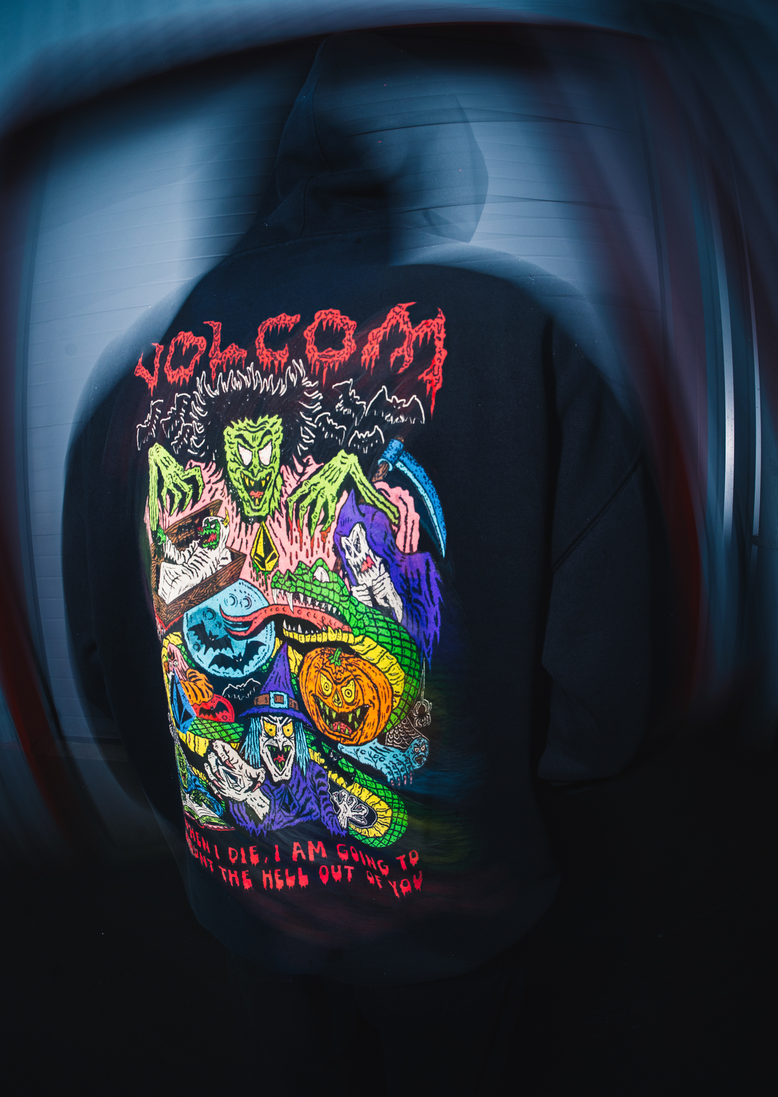 Black t-shirt with colourful horror-themed graphic featuring red "Volcom" text, green monster faces, blue and purple elements, orange pumpkin.