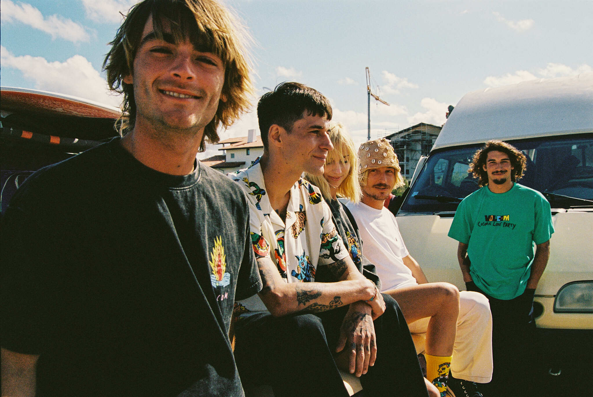 Four people posing for a photograph, smiling and standing in front of cars.