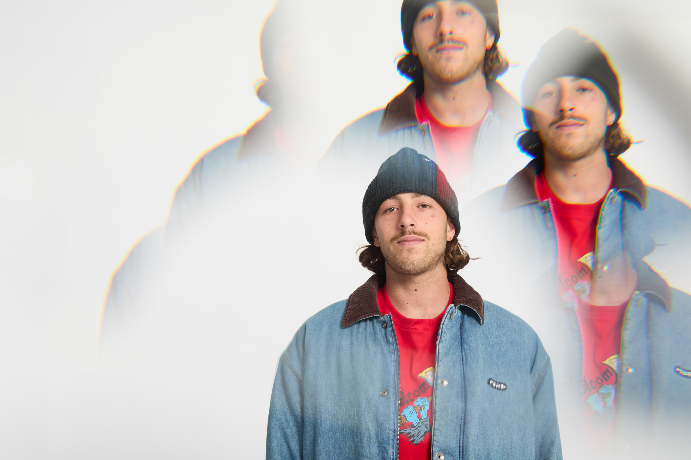 Man in blue denim shirt and red top with black beanie, multiple overlapping exposures creating prismatic light effects on white background.