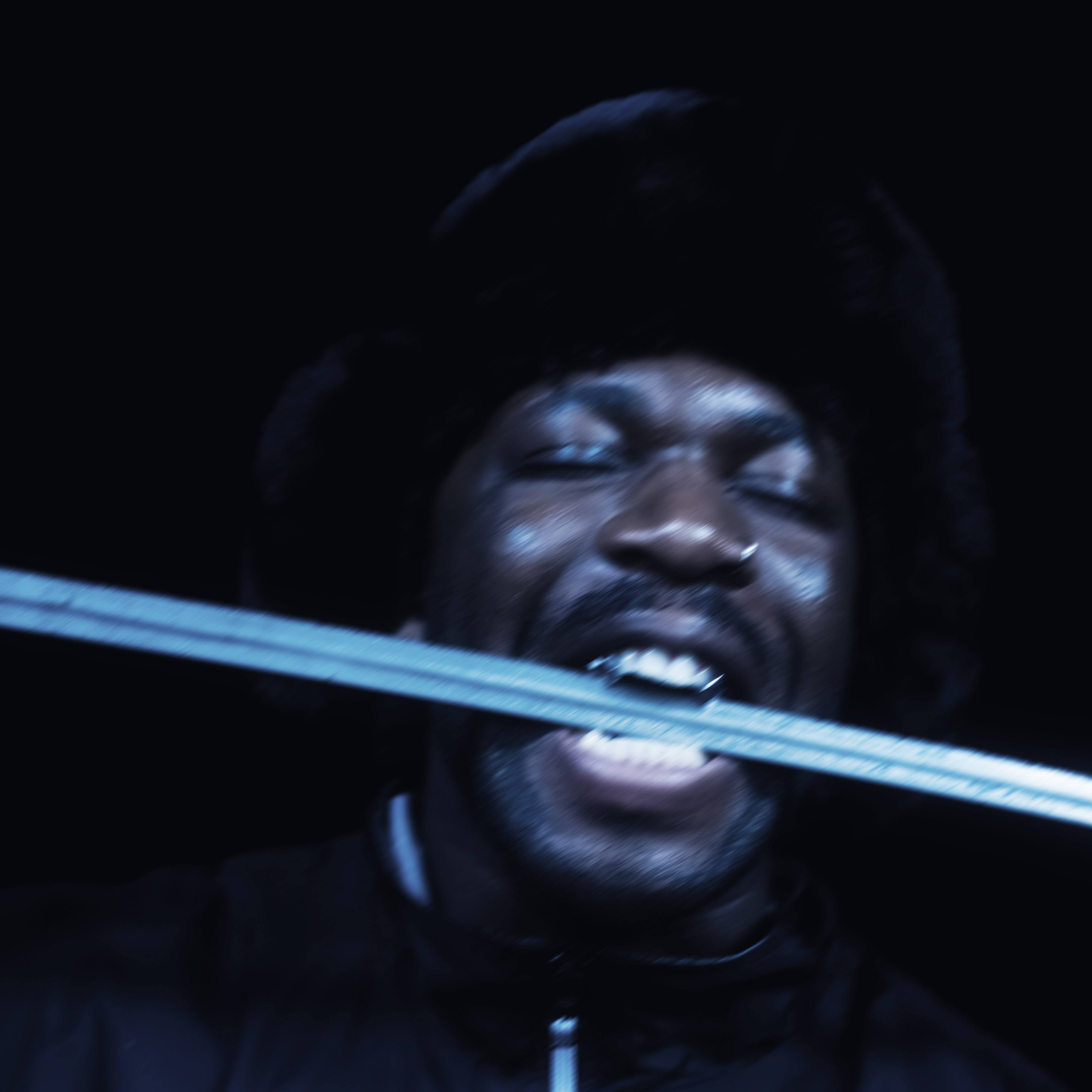 Close-up of a man with a stern expression and clenched teeth, illuminated in a dark, moody lighting.