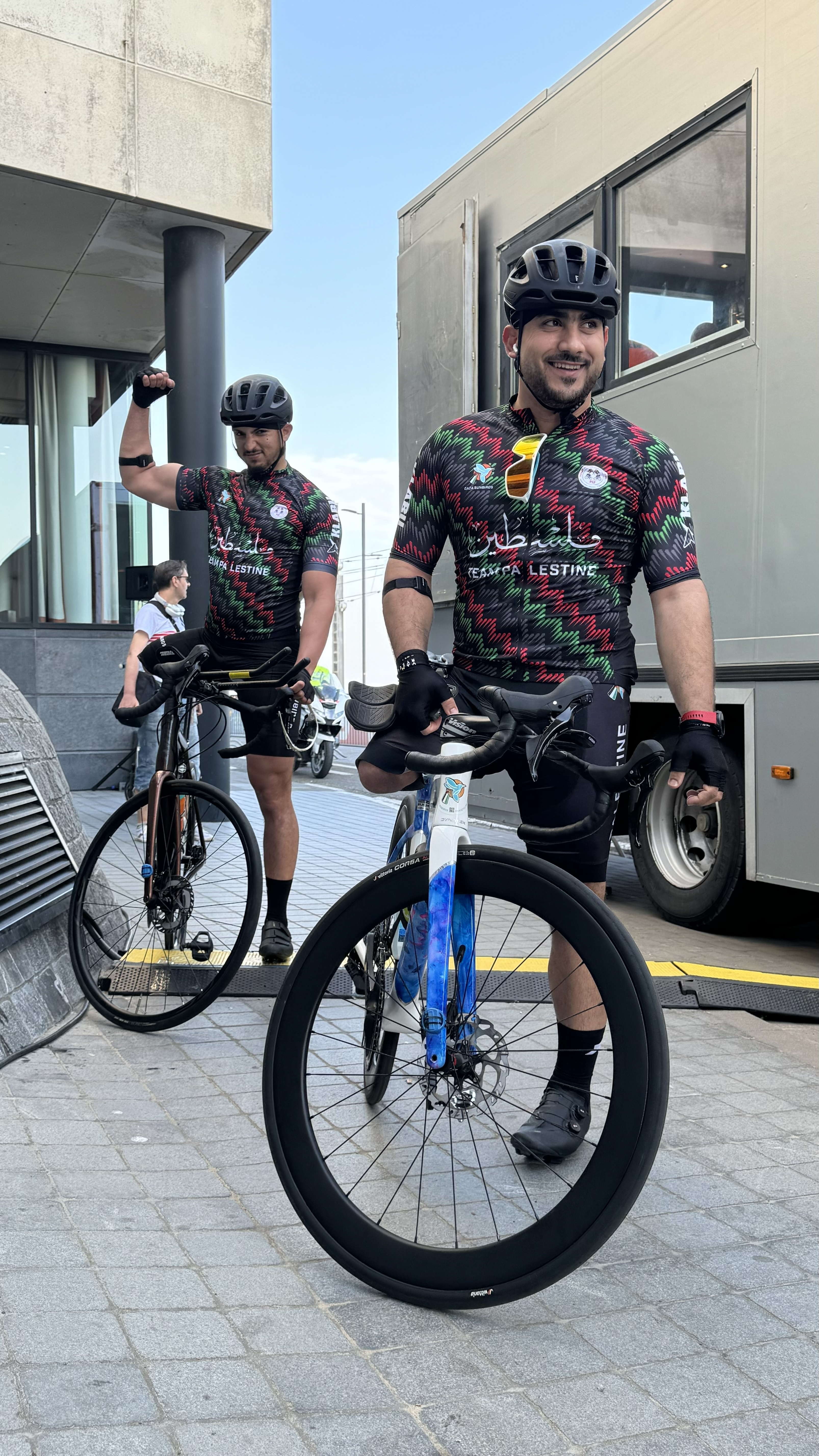Two cyclists wearing colourful jerseys and helmets standing next to road bikes.