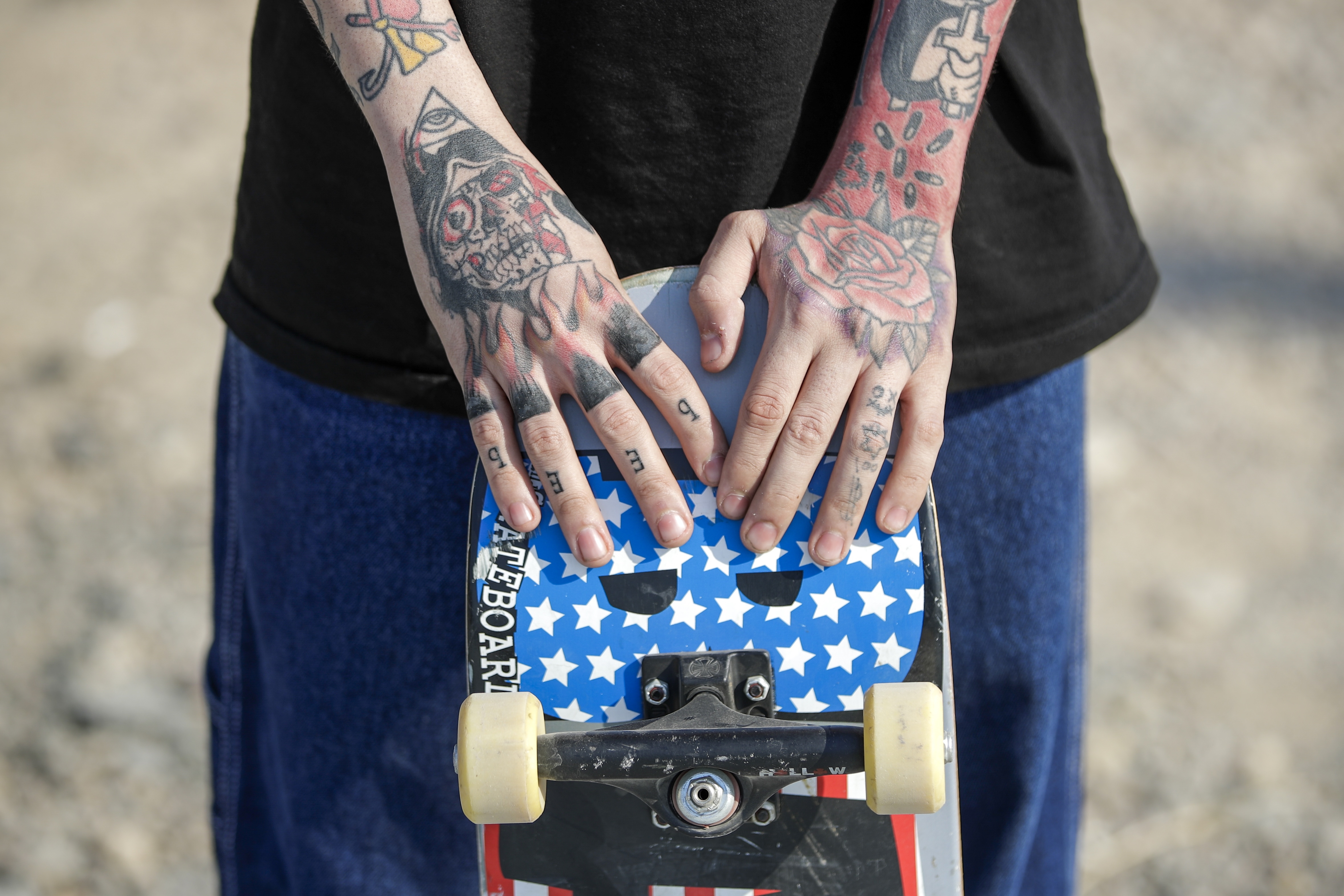Tattooed hands holding a star-patterned skateboard.